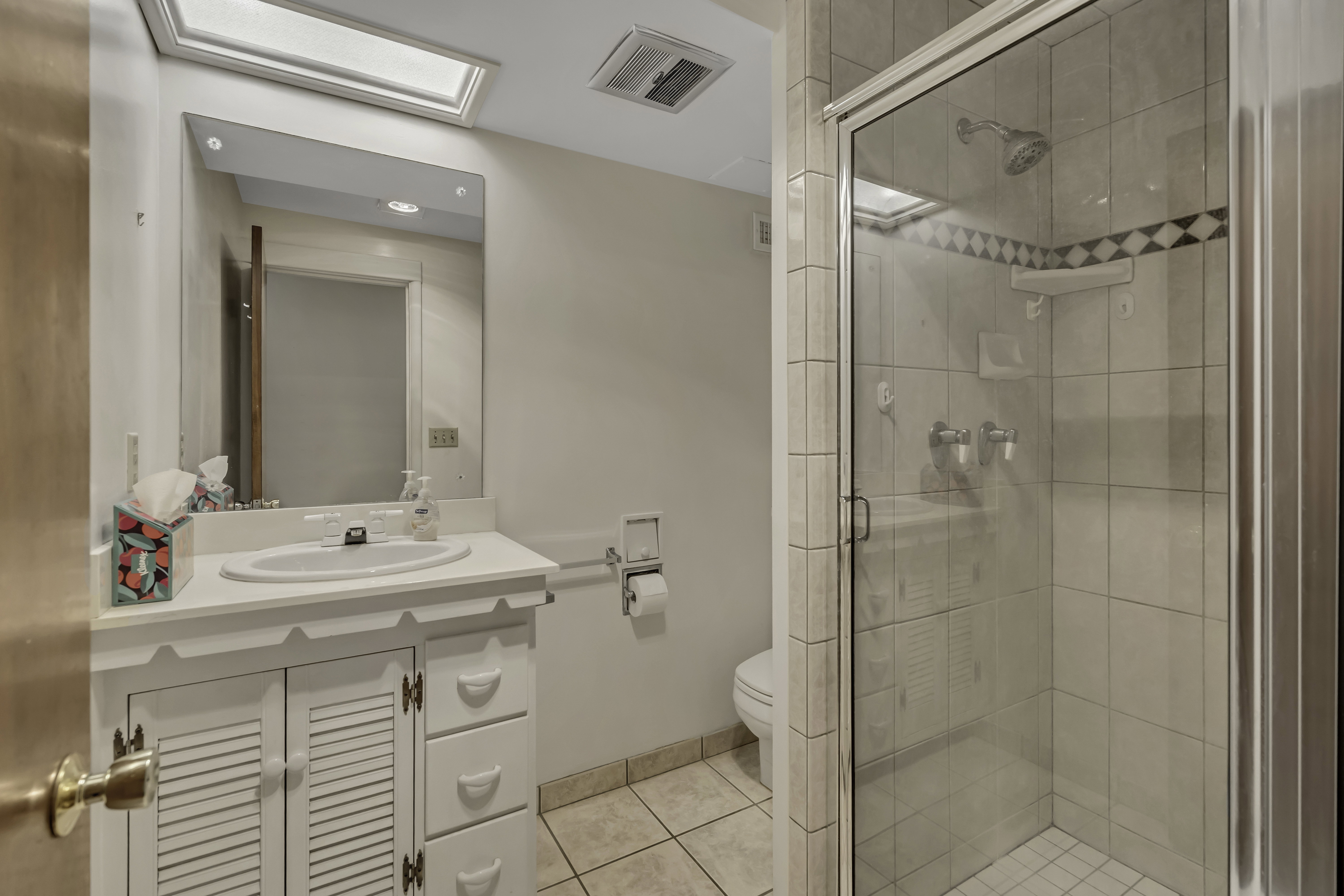 Full bathroom featuring a white vanity with integrated sink, glass-enclosed shower with tile surround, and a skylight