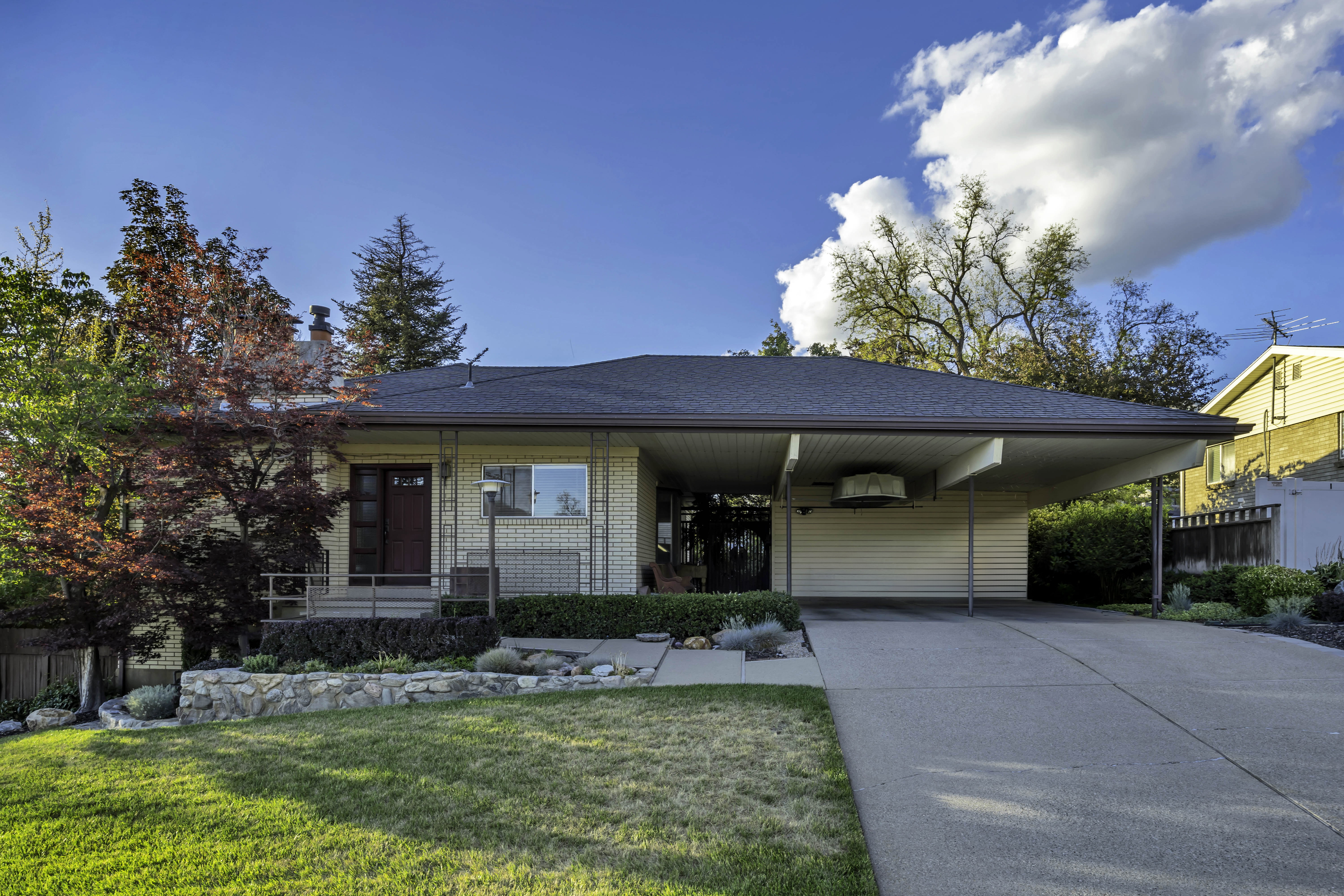 Single-story residence featuring light-colored brick siding, a dark asphalt shingle roof, and a covered carport