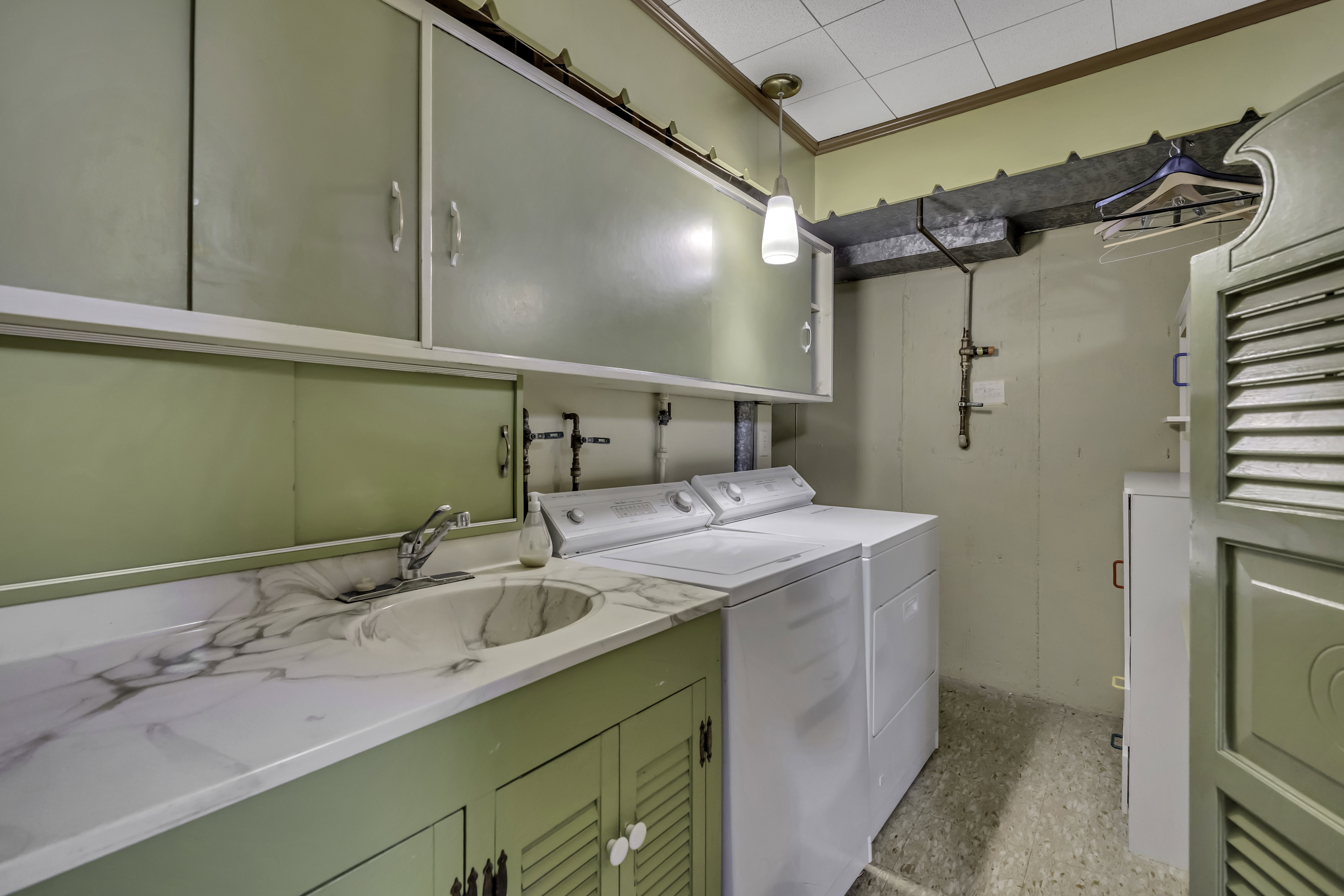 Laundry area featuring a built-in utility sink with stone-finish countertop, green cabinetry, and overhead storage