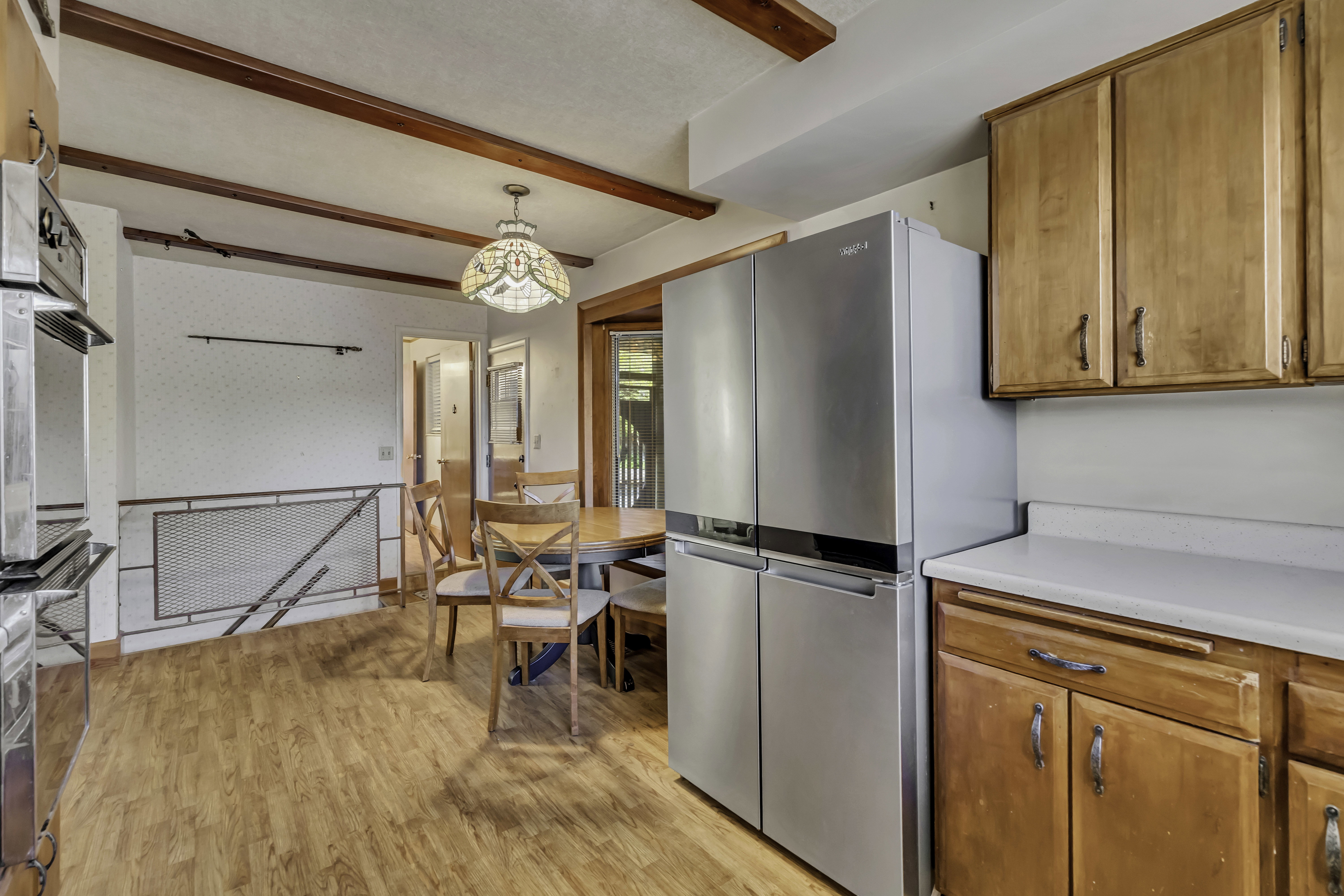 Kitchen and dining area featuring wood-finish flooring, exposed ceiling beams, and a stained glass-style ceiling fixture