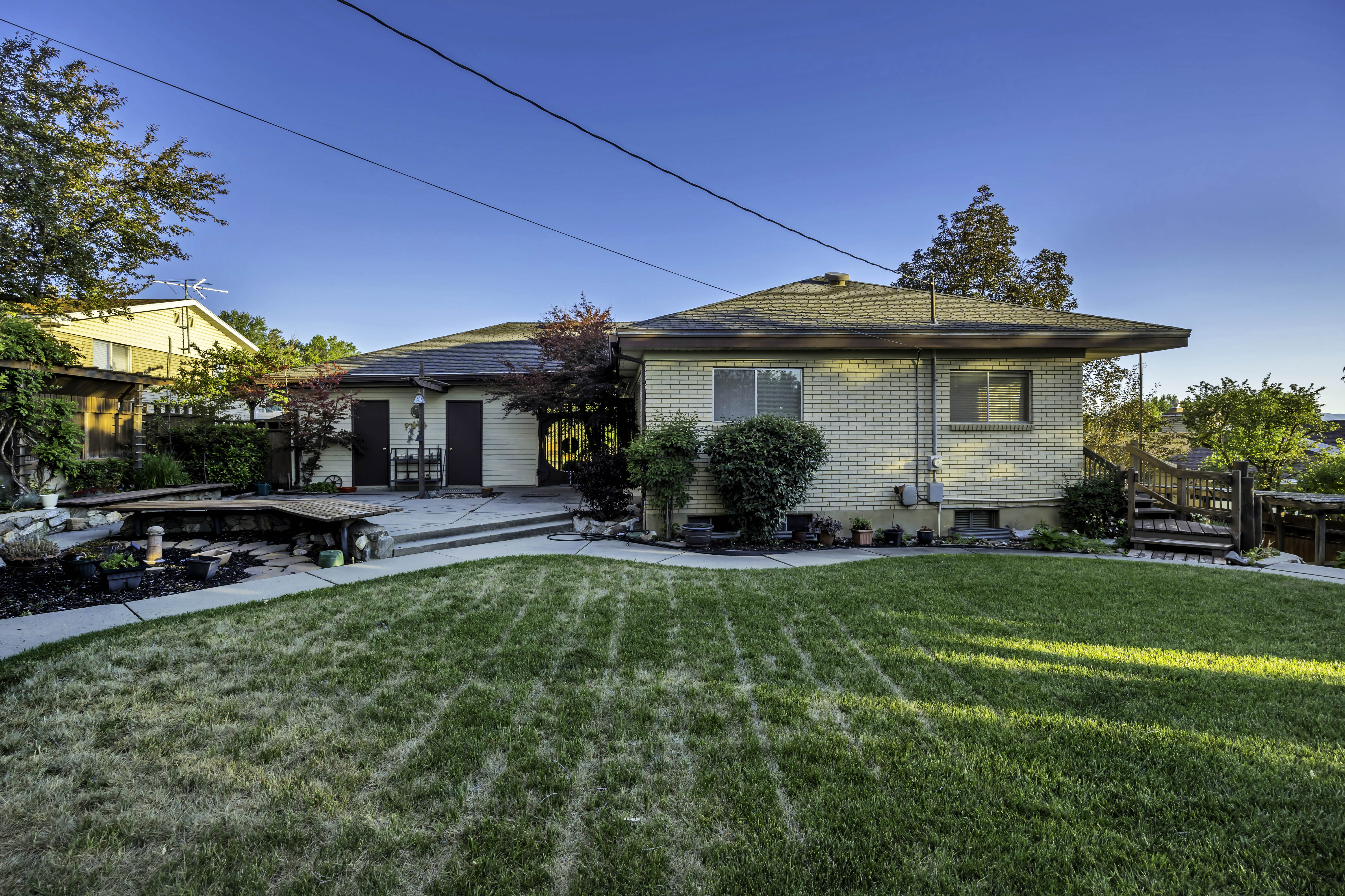 Expansive backyard featuring a partial stone paver patio, a raised wood deck, and a perimeter concrete pathway