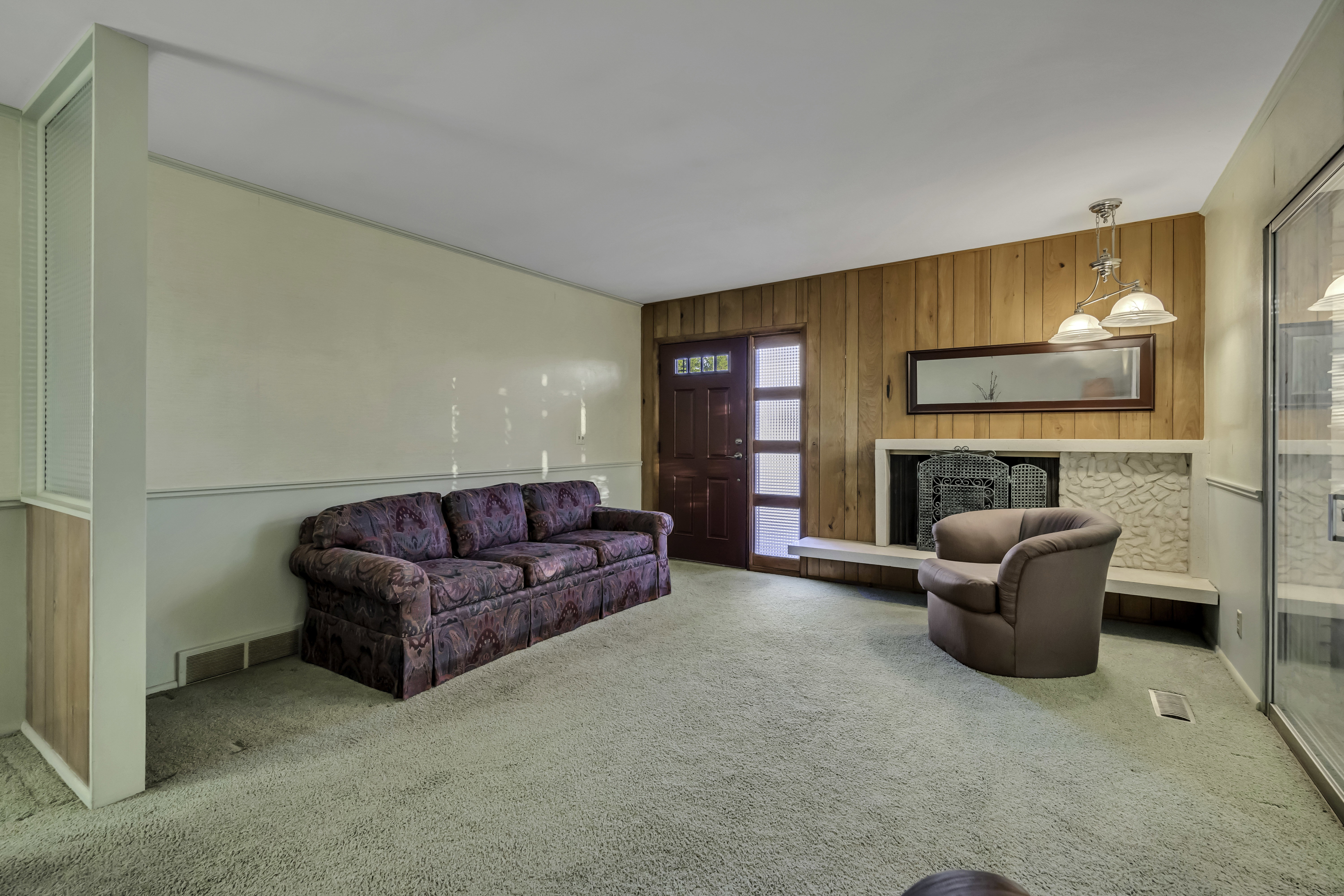 Living area featuring a textured carpet floor, a fireplace with a stone surround and hearth, a wood-paneled accent wall, and a multi-pane entry door with frosted glass inserts