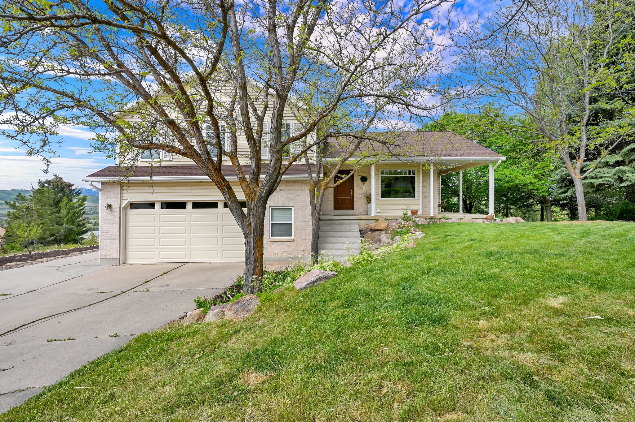 Two-story residence featuring a two-car garage, covered porch, concrete driveway, and mature landscaping