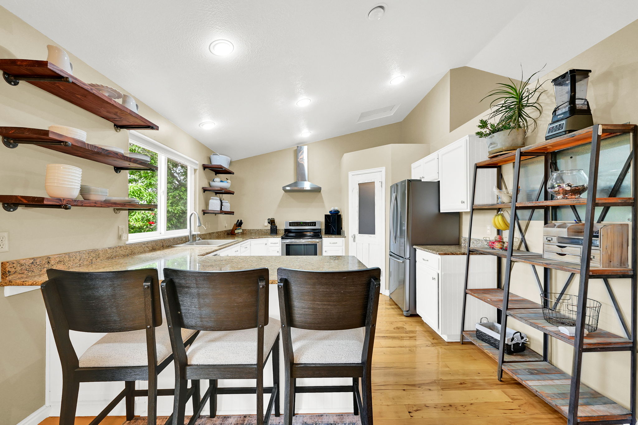Kitchen featuring open shelving, stainless steel appliances, a range hood, light-toned countertops, and wood-finish flooring