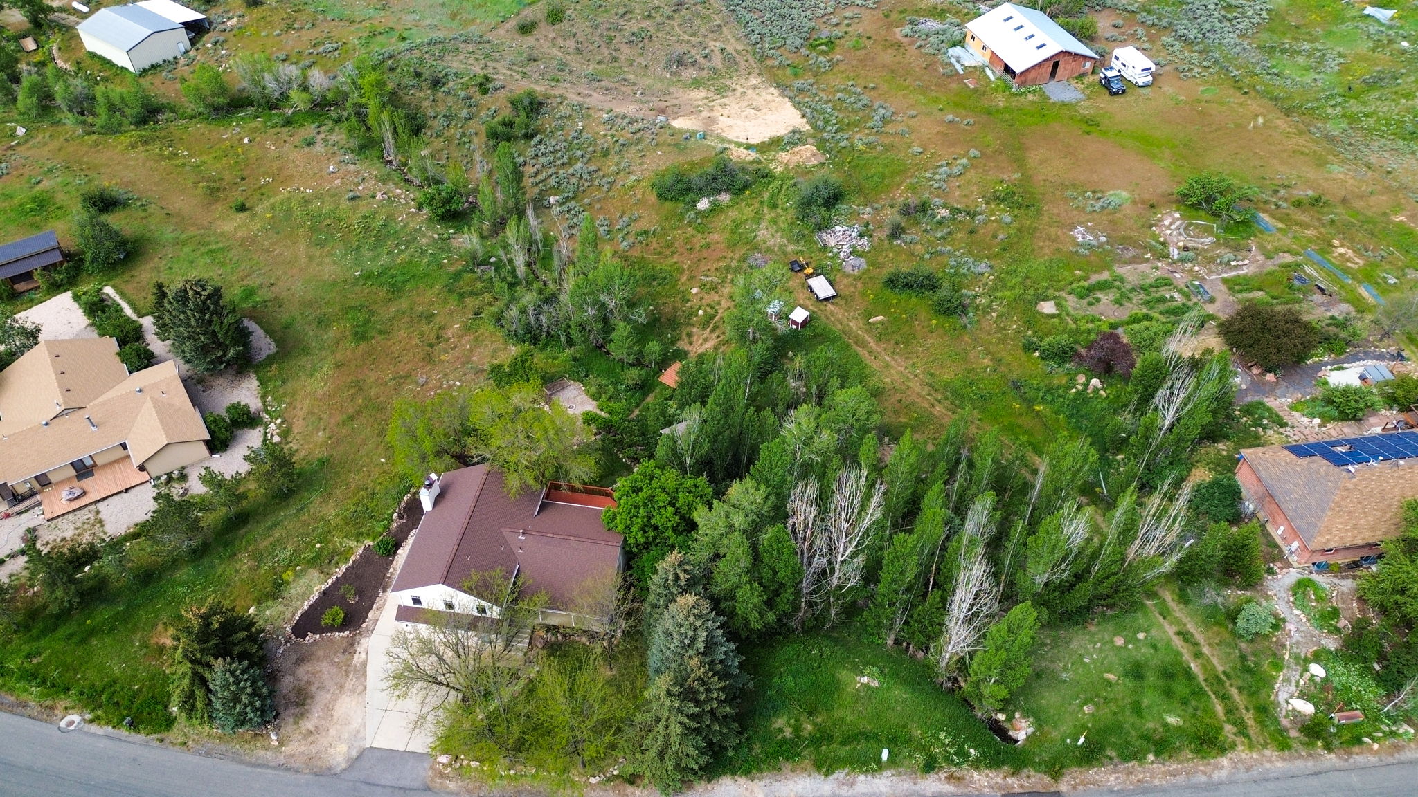 Expansive property featuring a brown roofline, mature trees, a paved driveway, and a partially visible deck