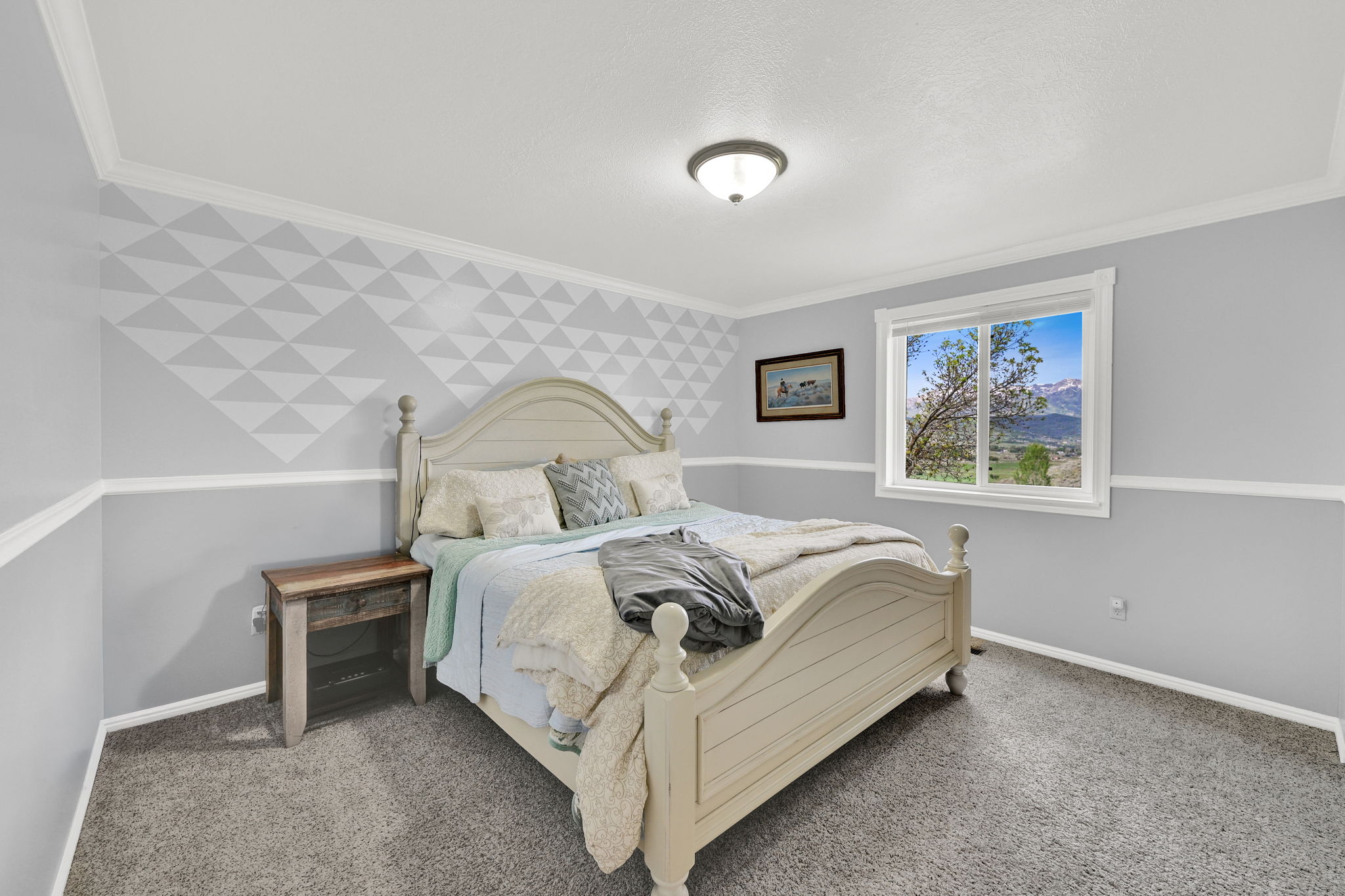 Carpeted room with a geometric accent wall featuring a chair rail, crown molding, and a window framing a mountainous landscape