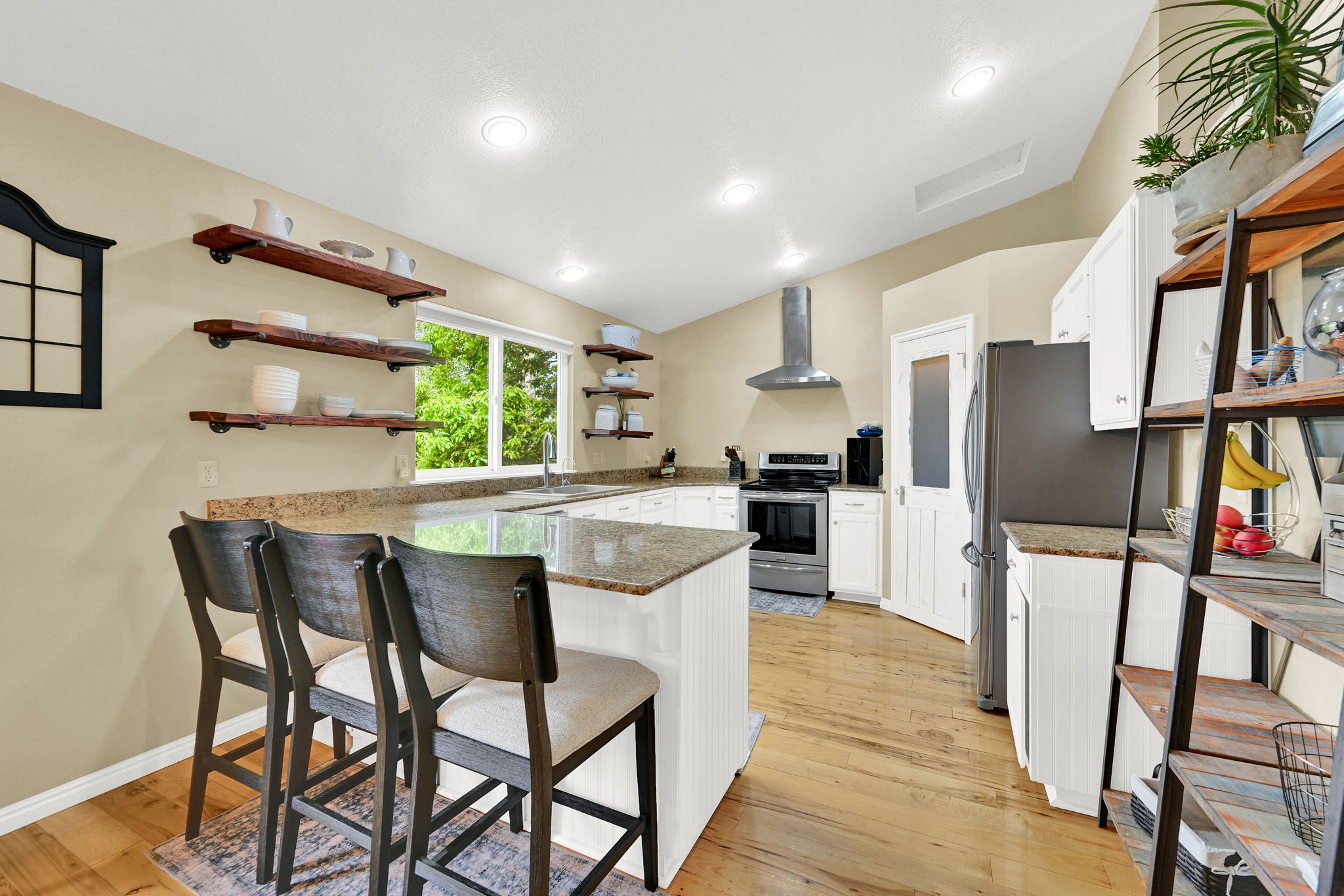 Kitchen featuring a granite-topped island with seating, white cabinetry, stainless steel appliances, wood-finish flooring, and recessed lighting