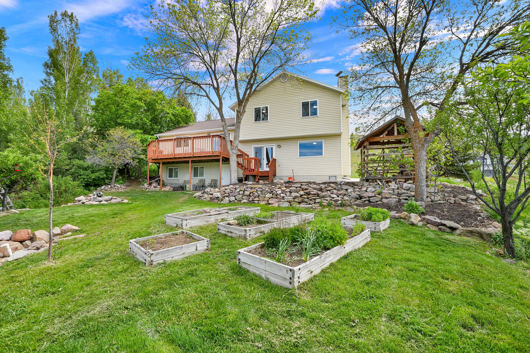 Expansive rear yard featuring multiple raised garden beds, a two-story residence with a second-story deck, a ground-level patio, and a separate gazebo structure