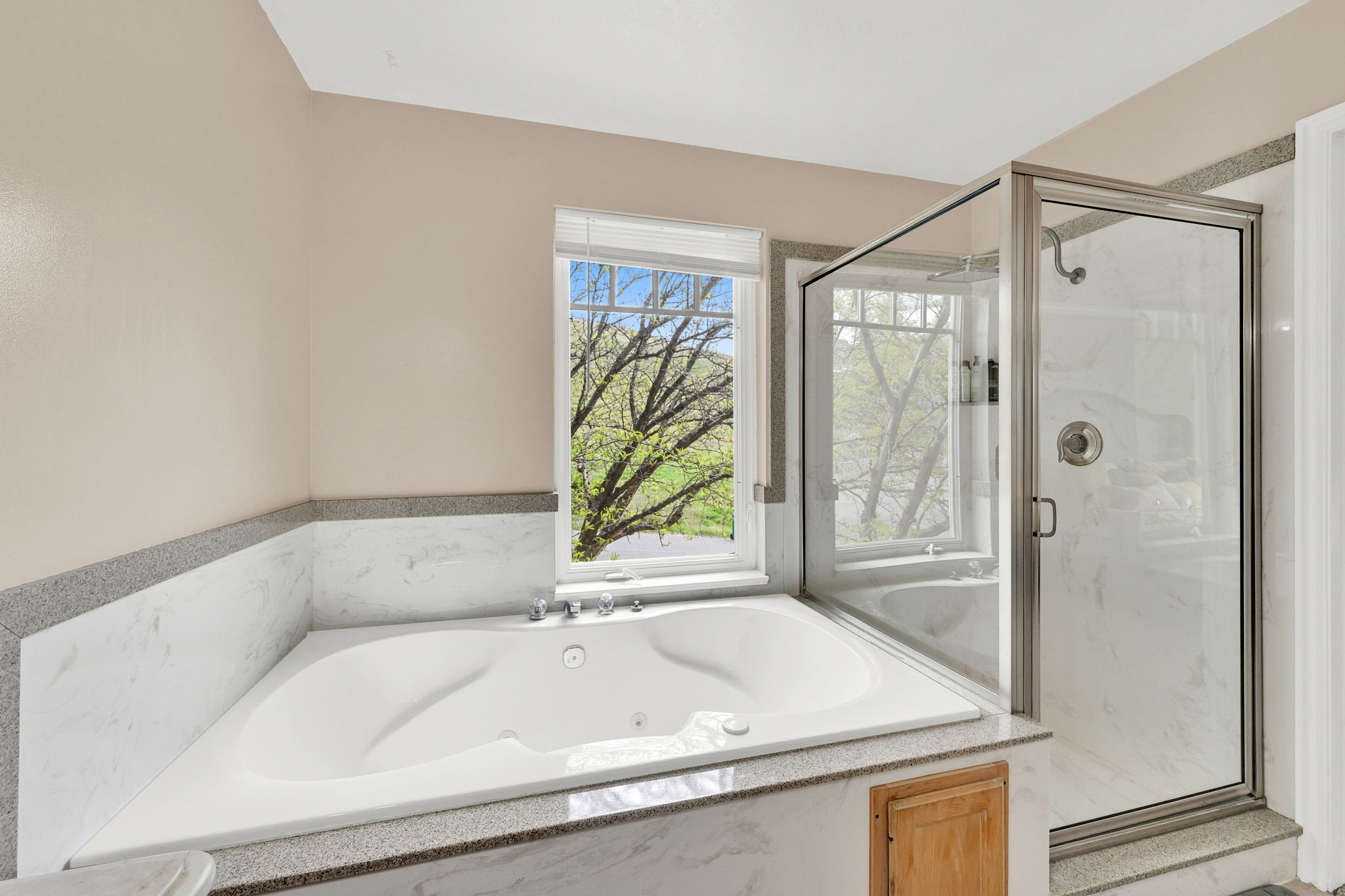 Corner jetted tub set within a marble surround with a granular countertop