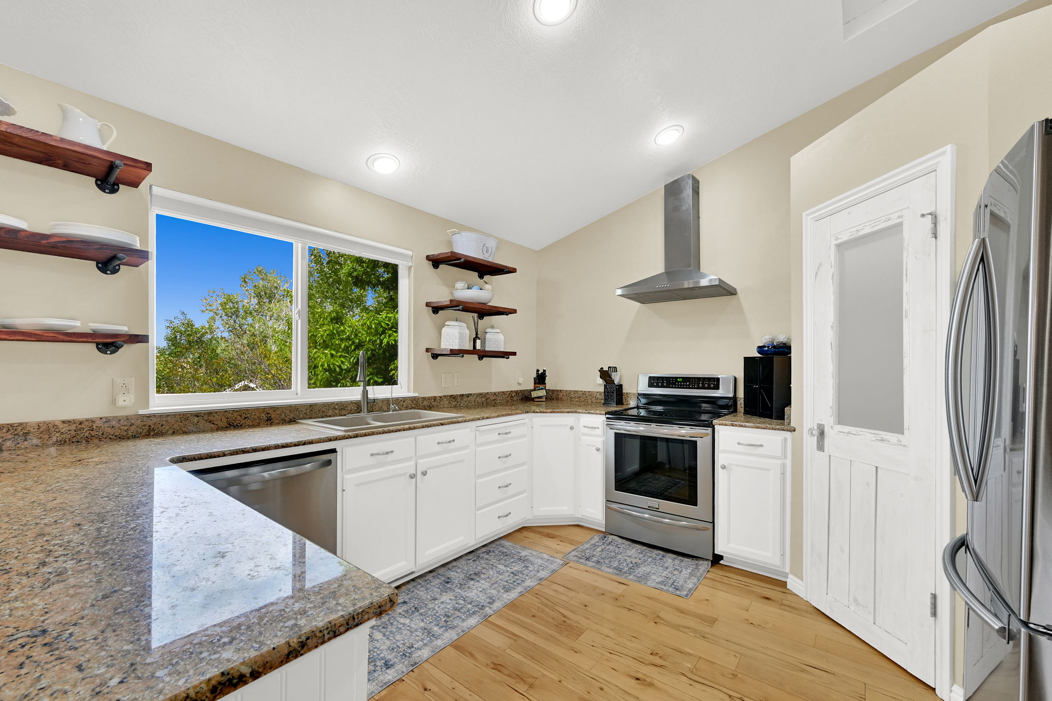 Modern kitchen featuring wood-finish flooring, white cabinetry, granite countertops, and stainless steel appliances