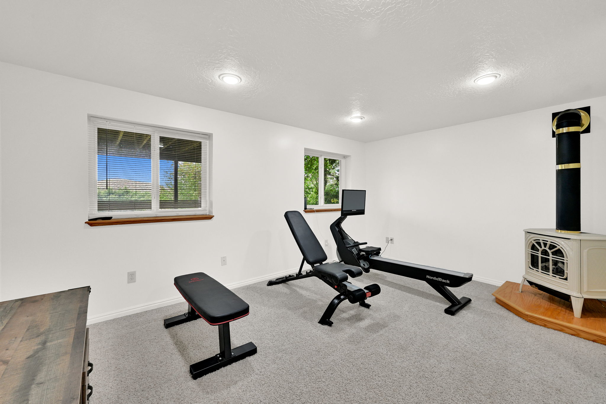 Spacious room featuring light gray carpeting, recessed ceiling lighting, a cream-colored freestanding stove with a black stovepipe, and white walls