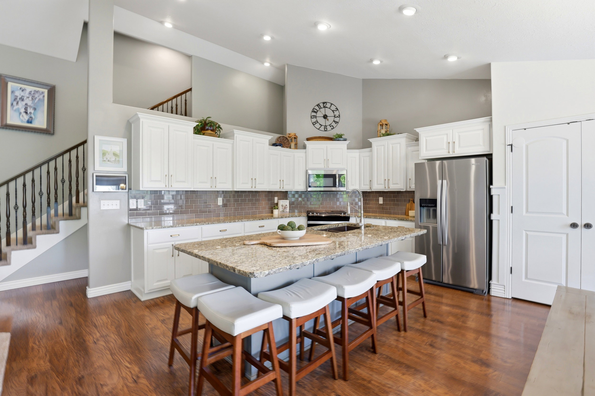 Spacious kitchen featuring an expansive center island with seating, wood-finish flooring, white cabinetry, stainless steel appliances, and a tile backsplash