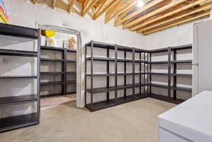 Utility room featuring extensive built-in shelving, exposed ceiling joists, concrete flooring, and an additional storage area