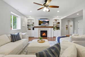 Living area featuring a fireplace with a wood mantle and shiplap accents, built-in shelving and cabinetry, recessed lighting, and a ceiling fan