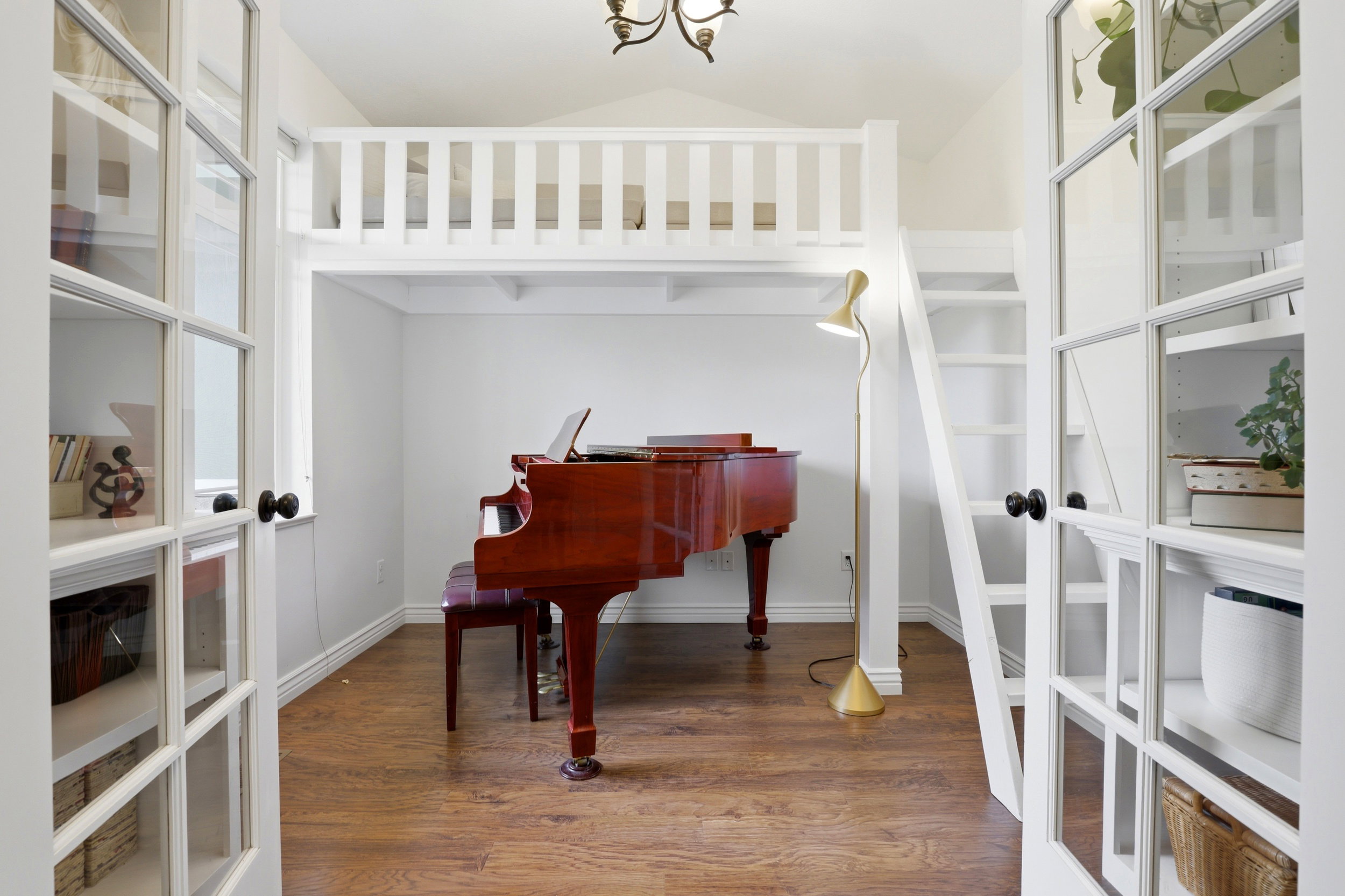 Room featuring a white painted loft area with railing and ladder, wood-finish flooring, and white walls