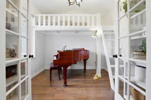 Room featuring a white painted loft area with railing and ladder, wood-finish flooring, and white walls