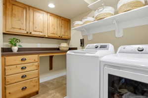 Laundry area featuring natural wood cabinetry, integrated countertop space, upper storage shelving, and tile flooring