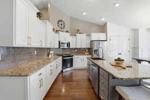 Kitchen featuring white cabinetry with gold-toned hardware, an expansive island with a sink, stainless steel appliances, granite countertops, and wood-finish flooring
