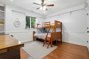 Room featuring wood-finish flooring, built-in shelving, a window, crown molding, and a ceiling fan with integrated lighting