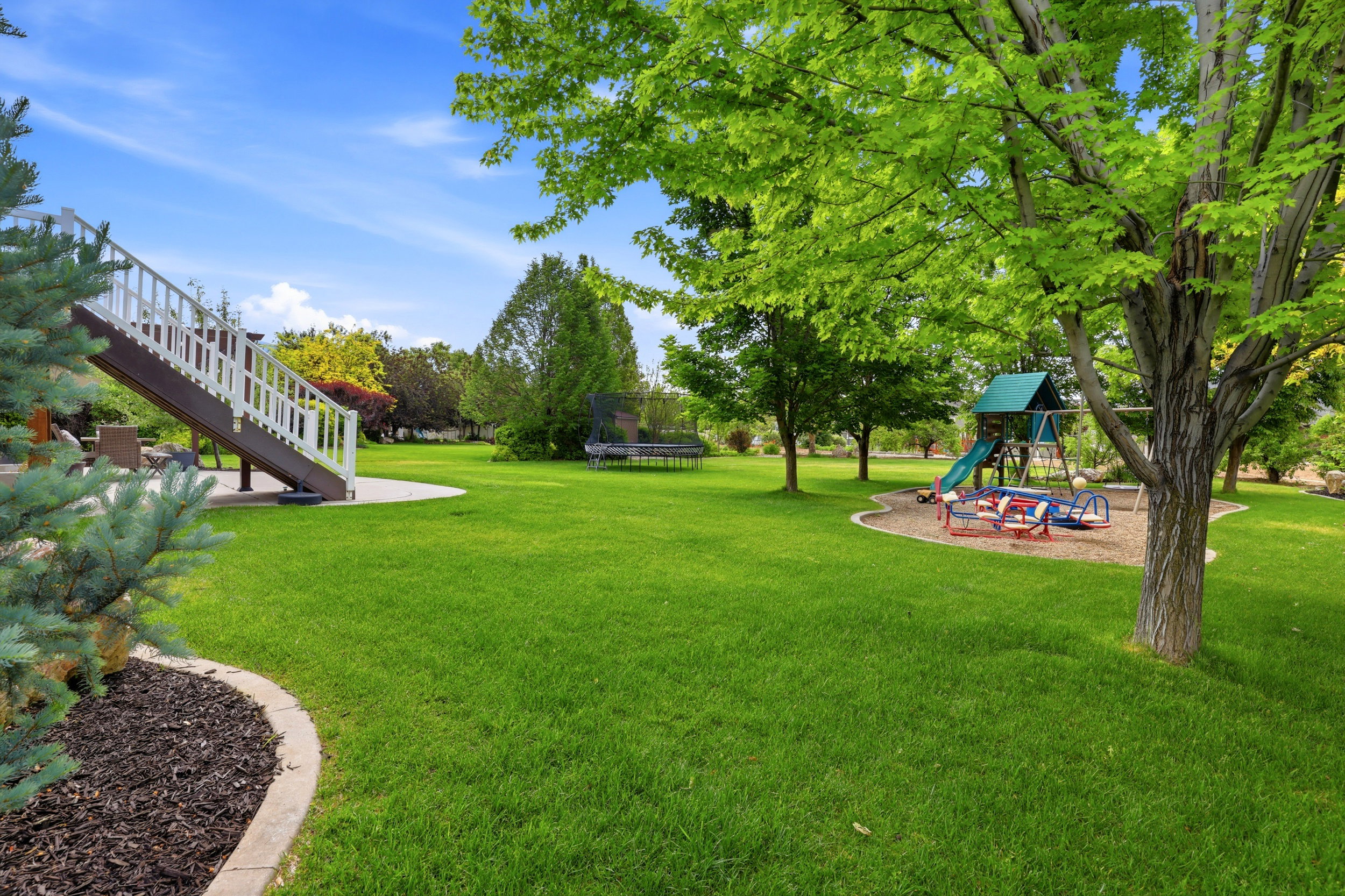 Expansive green lawn with mature trees, featuring a concrete patio with stairs, and a designated play area