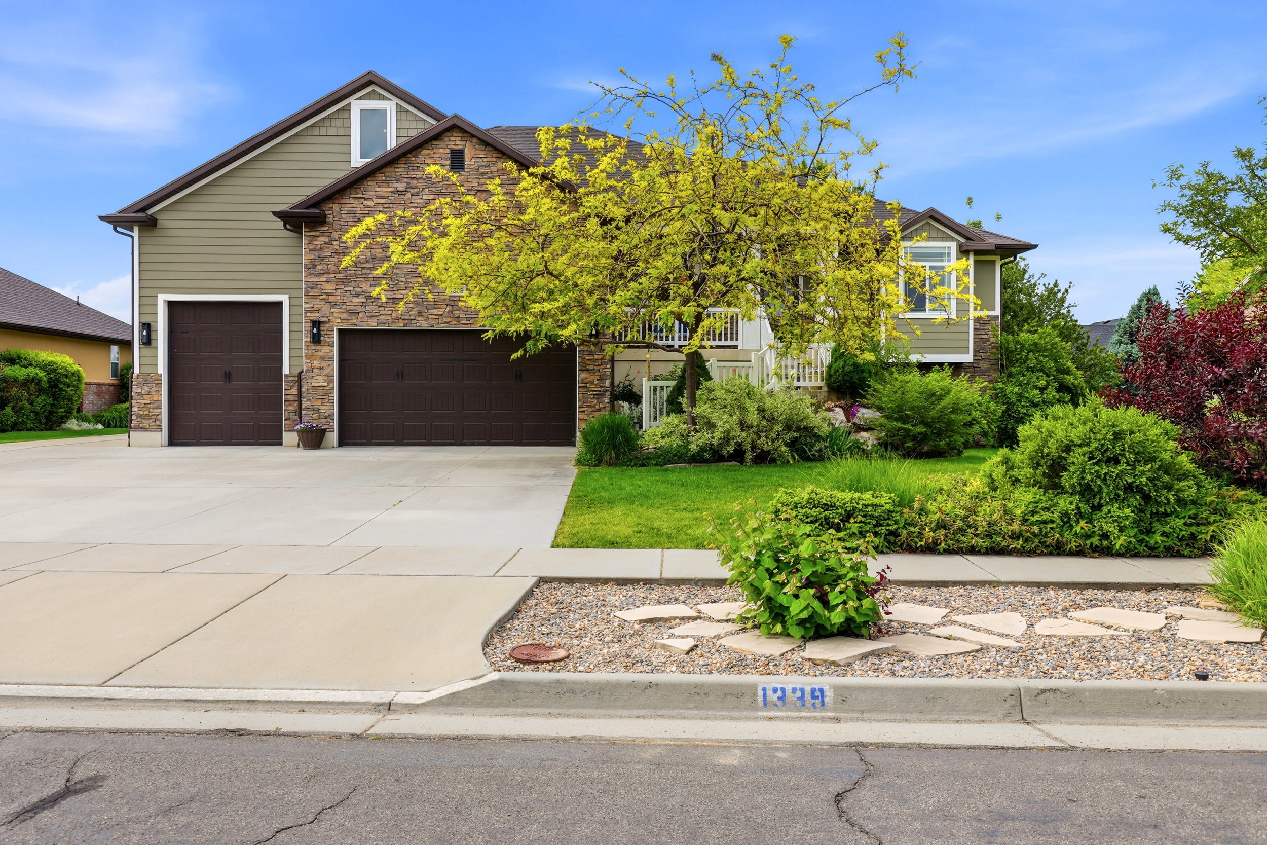 Crafted stone and siding exterior featuring two attached garage doors, a concrete driveway, and mature front landscaping