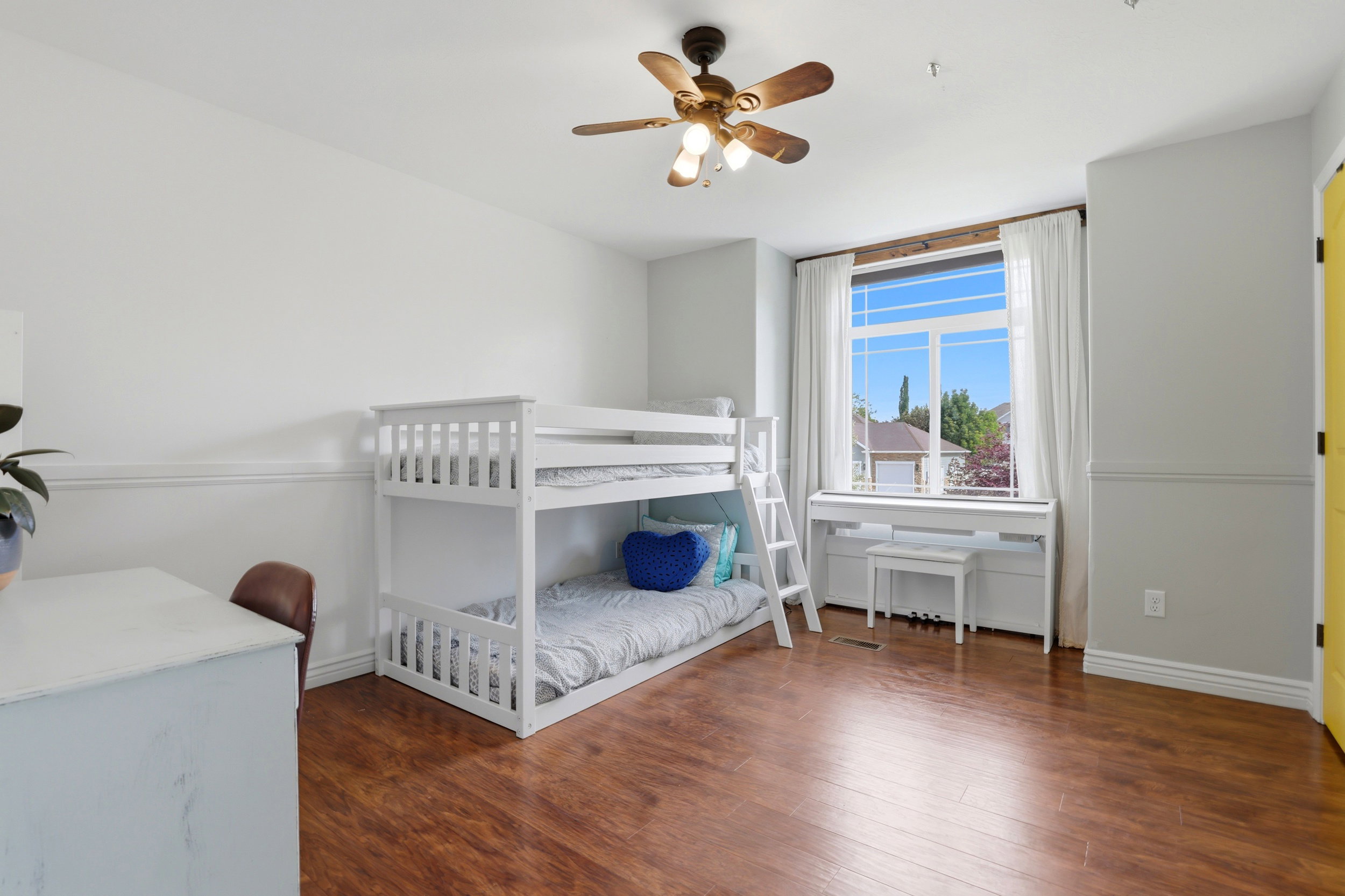 Bright room featuring wood-finish flooring, a large window with white trim and drapes, and a ceiling fan with integrated lighting