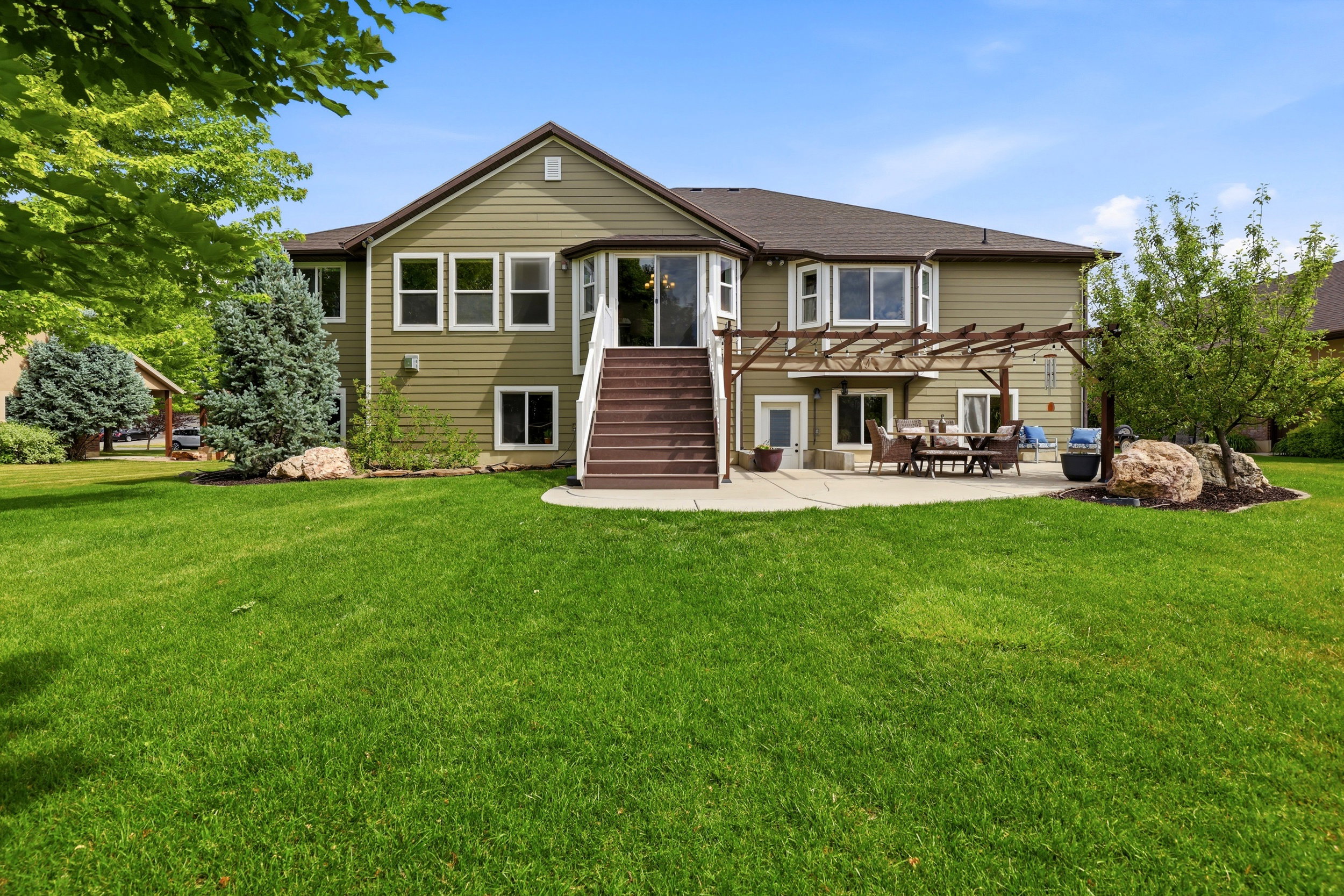 Expansive green lawn bordering a residence with olive-toned siding and white trim