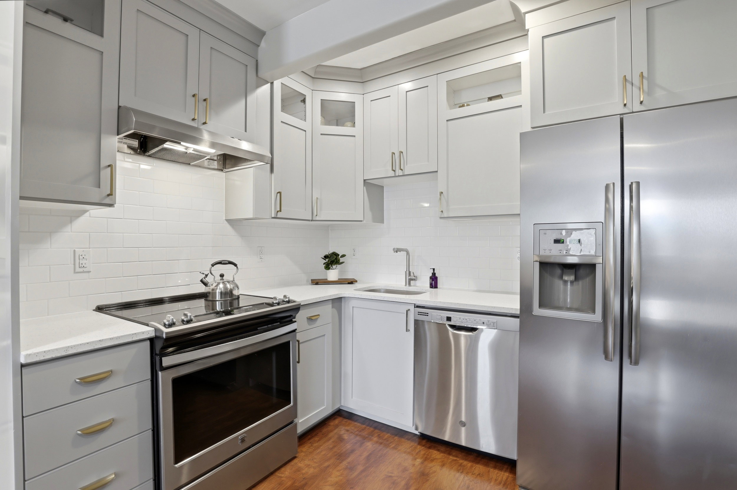 Modern kitchen featuring gray shaker-style cabinetry, stainless steel appliances, white subway tile backsplash, light-colored countertops, and wood-finish flooring