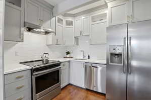 Modern kitchen featuring gray shaker-style cabinetry, stainless steel appliances, white subway tile backsplash, light-colored countertops, and wood-finish flooring