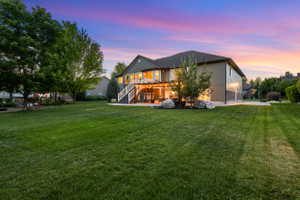 Expansive green lawn with mature trees, a two-story home featuring a second-story deck, a covered patio, and stone accents on the lower facade