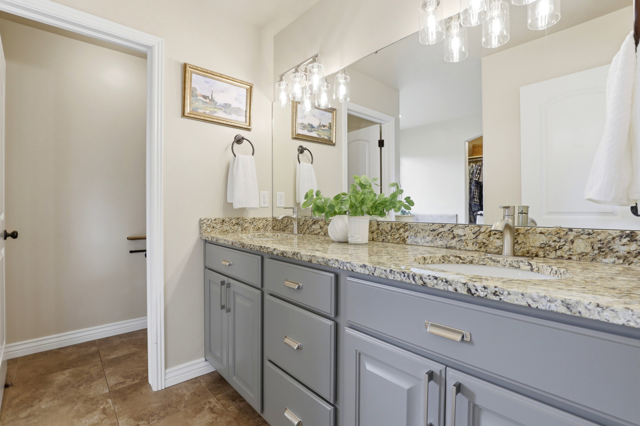 Dual sink vanity with grey cabinetry, stone countertop, brushed nickel fixtures, and integrated lighting