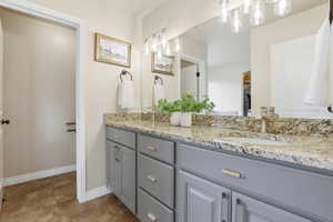 Dual sink vanity with grey cabinetry, stone countertop, brushed nickel fixtures, and integrated lighting