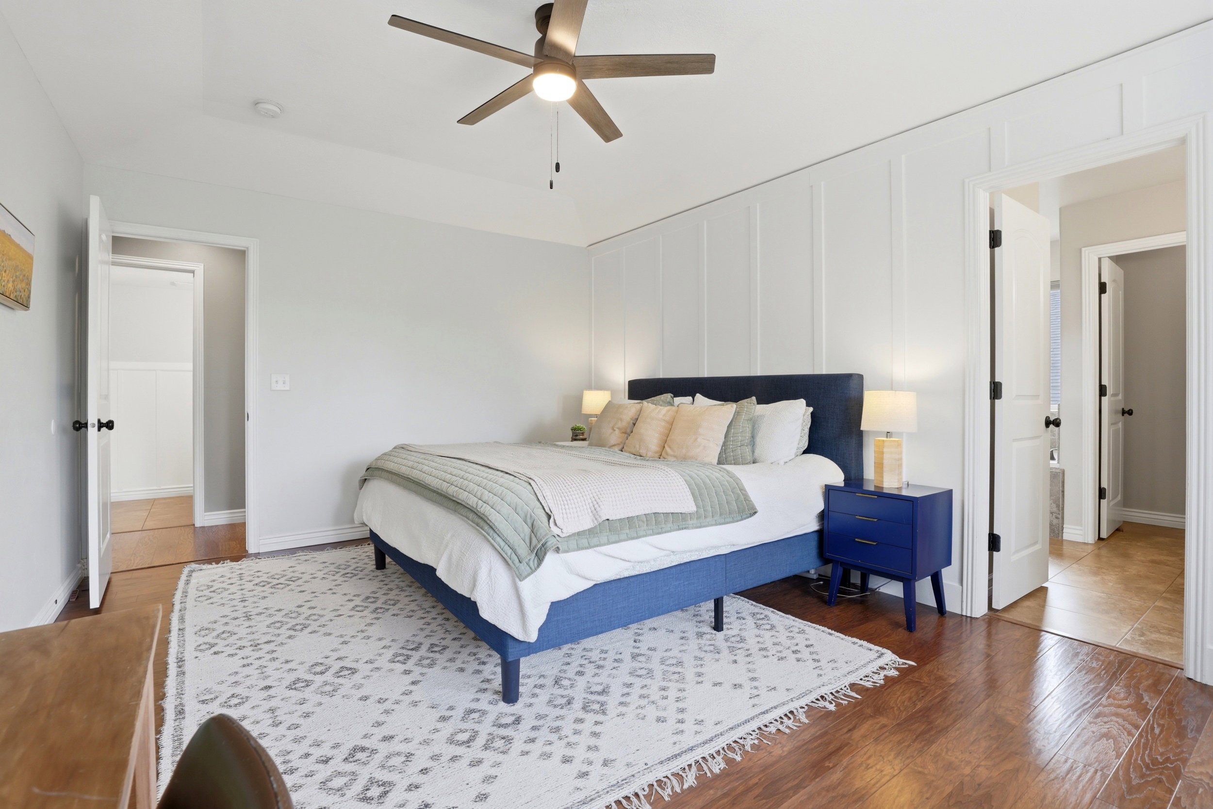 Bedroom featuring wood-finish flooring, a decorative accent wall with vertical paneling, and a ceiling fan with integrated lighting