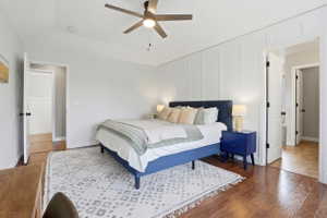 Bedroom featuring wood-finish flooring, a decorative accent wall with vertical paneling, and a ceiling fan with integrated lighting