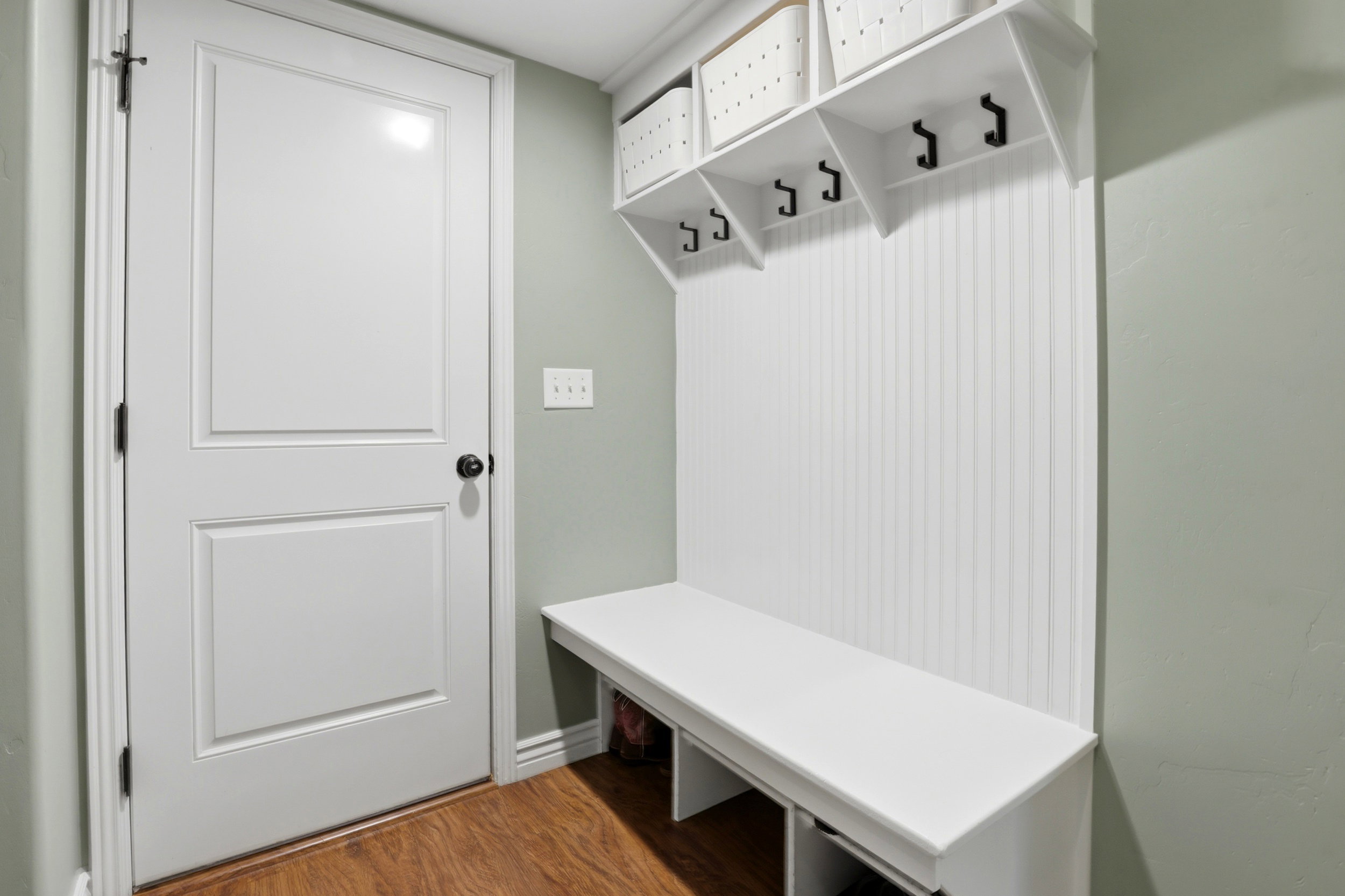 Entryway mudroom featuring a built-in white bench and upper shelving, beadboard paneling, and four black coat hooks
