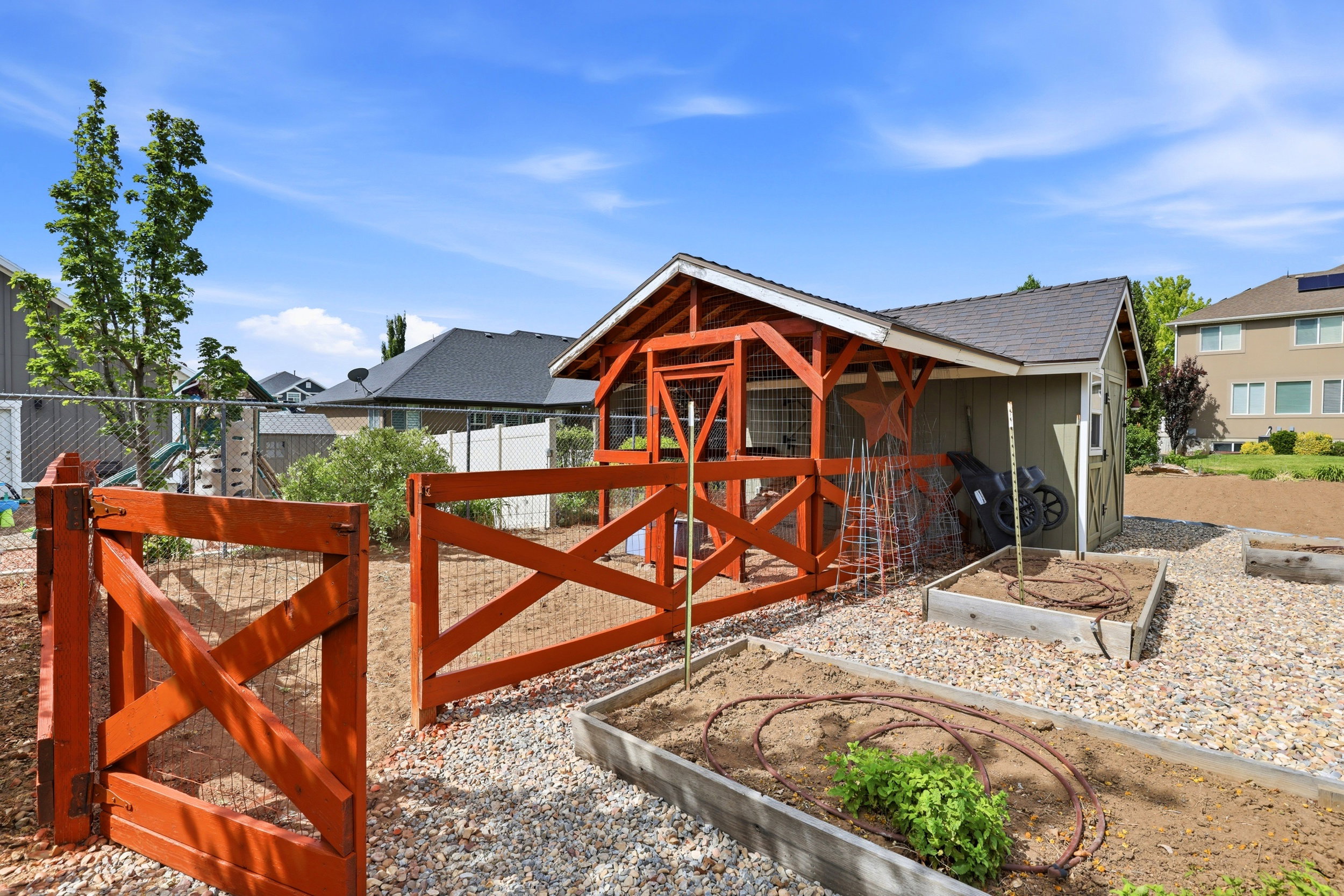 Rear yard featuring a green storage shed with a dark shingle roof, accompanied by an open-air structure with a red wood frame