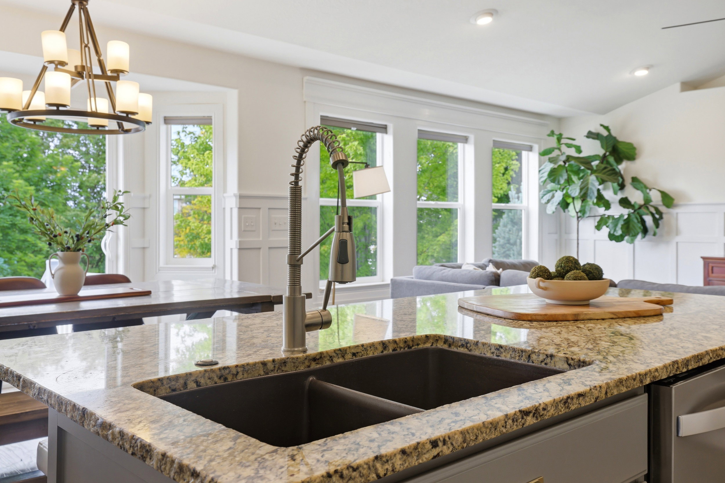 Kitchen island featuring a granite countertop, dual basin sink with pull-down faucet, and integrated dishwasher