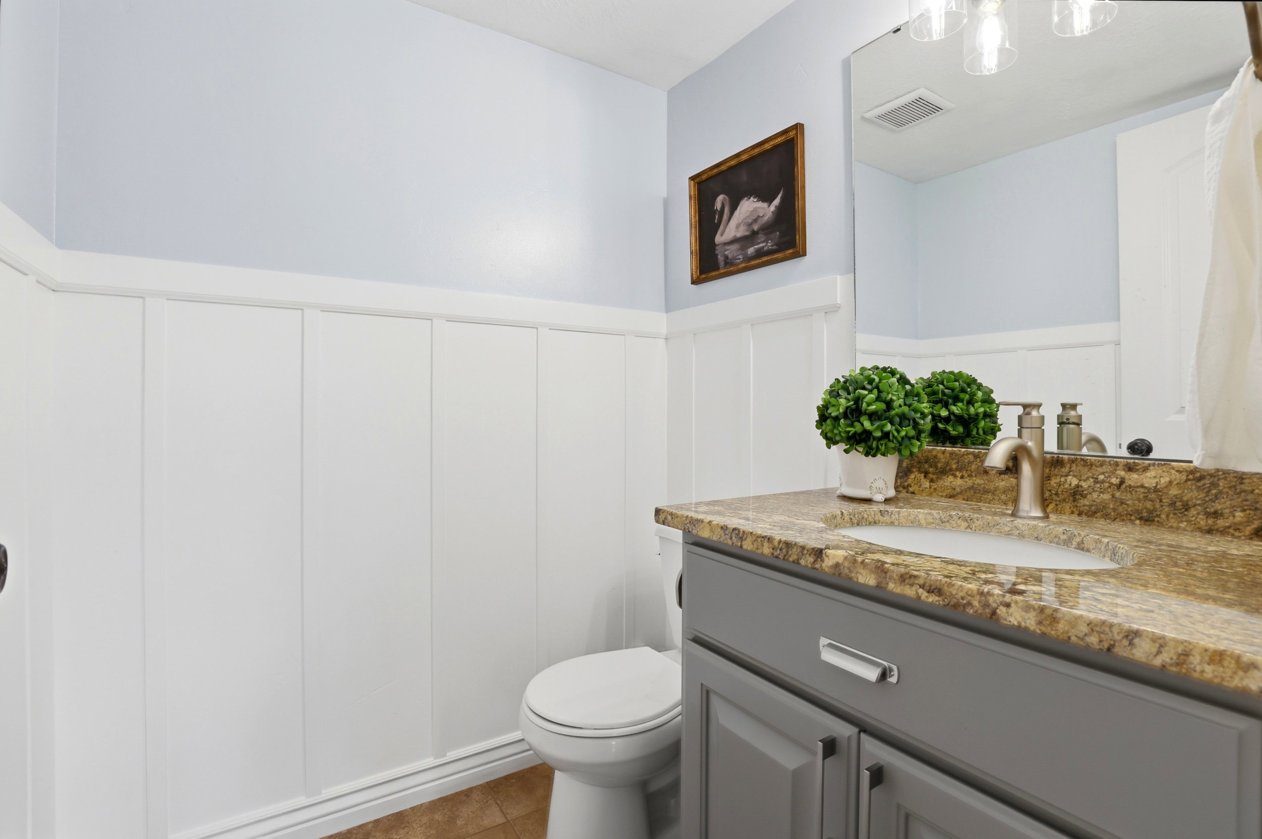 Bathroom featuring wainscoting, light blue wall paint, a vanity with a stone-finish countertop, an undermount sink, and a framed mirror