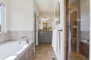 Bathroom featuring a built-in tub with tile surround, a separate glass-enclosed shower, a vanity with a stone-finish countertop, and tile flooring