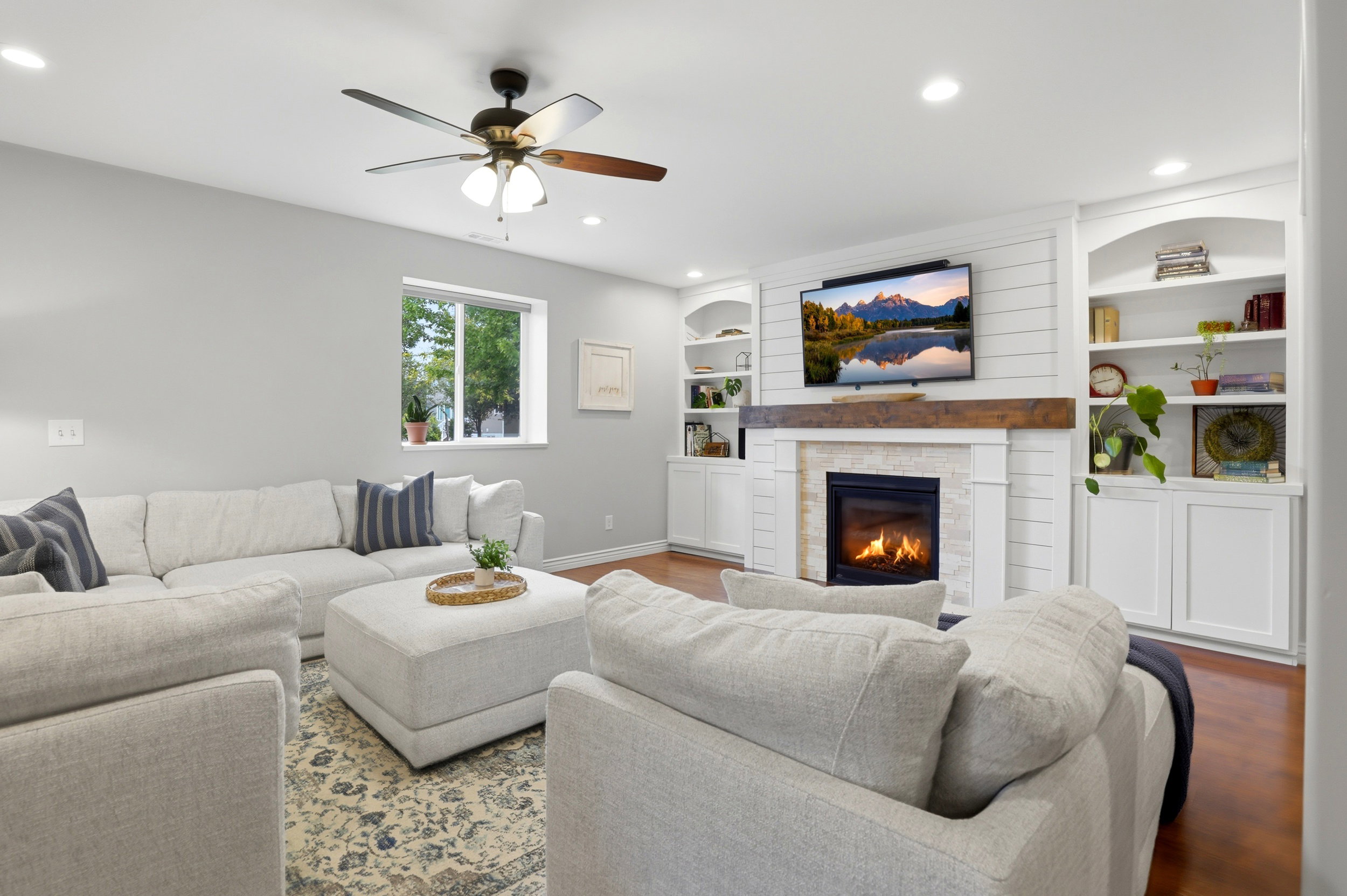 Living area featuring a gas fireplace with stone surround, shiplap accent wall, built-in shelving, wood-finish flooring, and recessed lighting