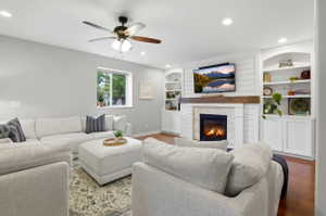 Living area featuring a gas fireplace with stone surround, shiplap accent wall, built-in shelving, wood-finish flooring, and recessed lighting
