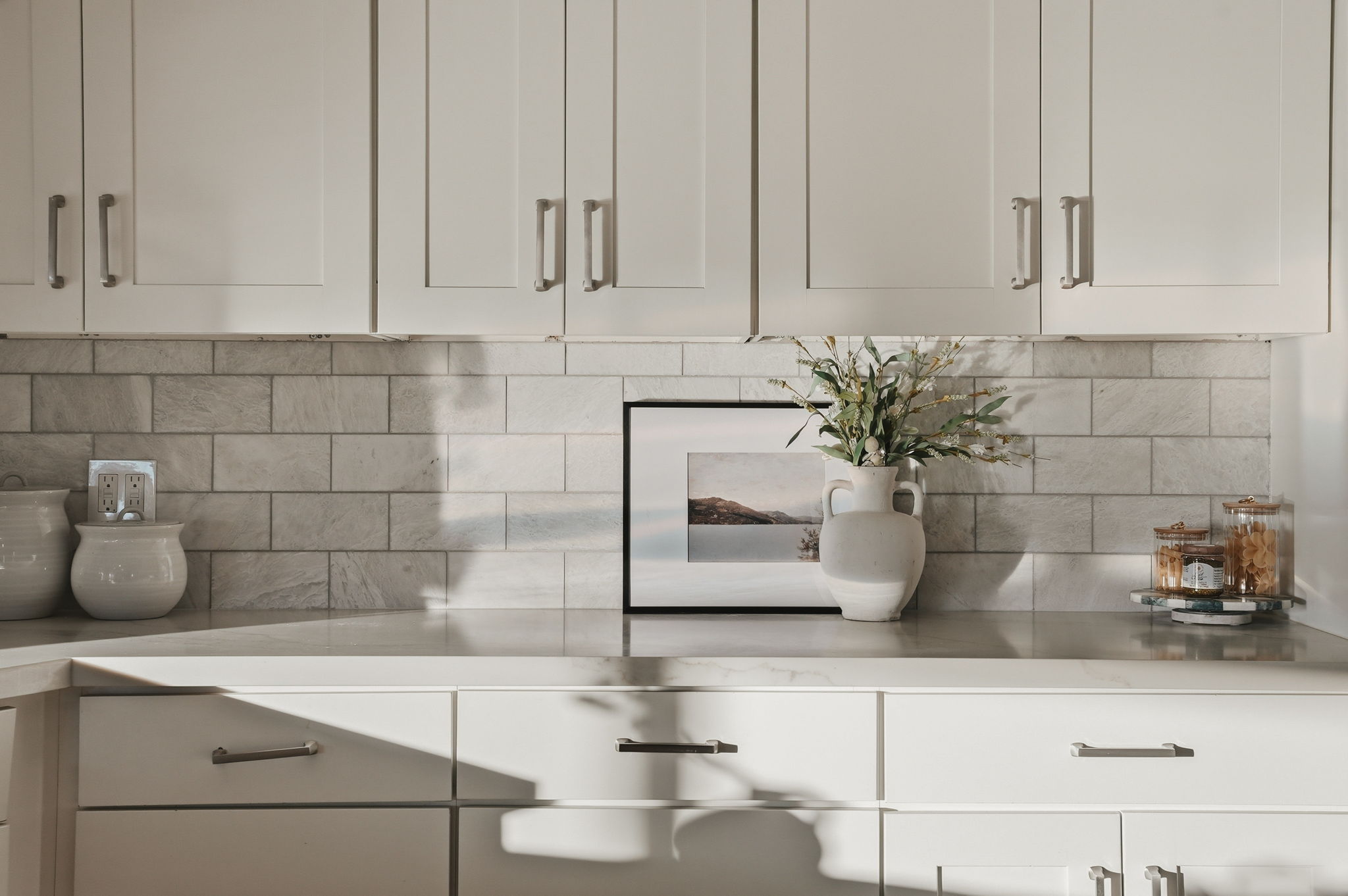 White shaker-style cabinetry with brushed nickel hardware, light-toned countertop, and subway tile backsplash