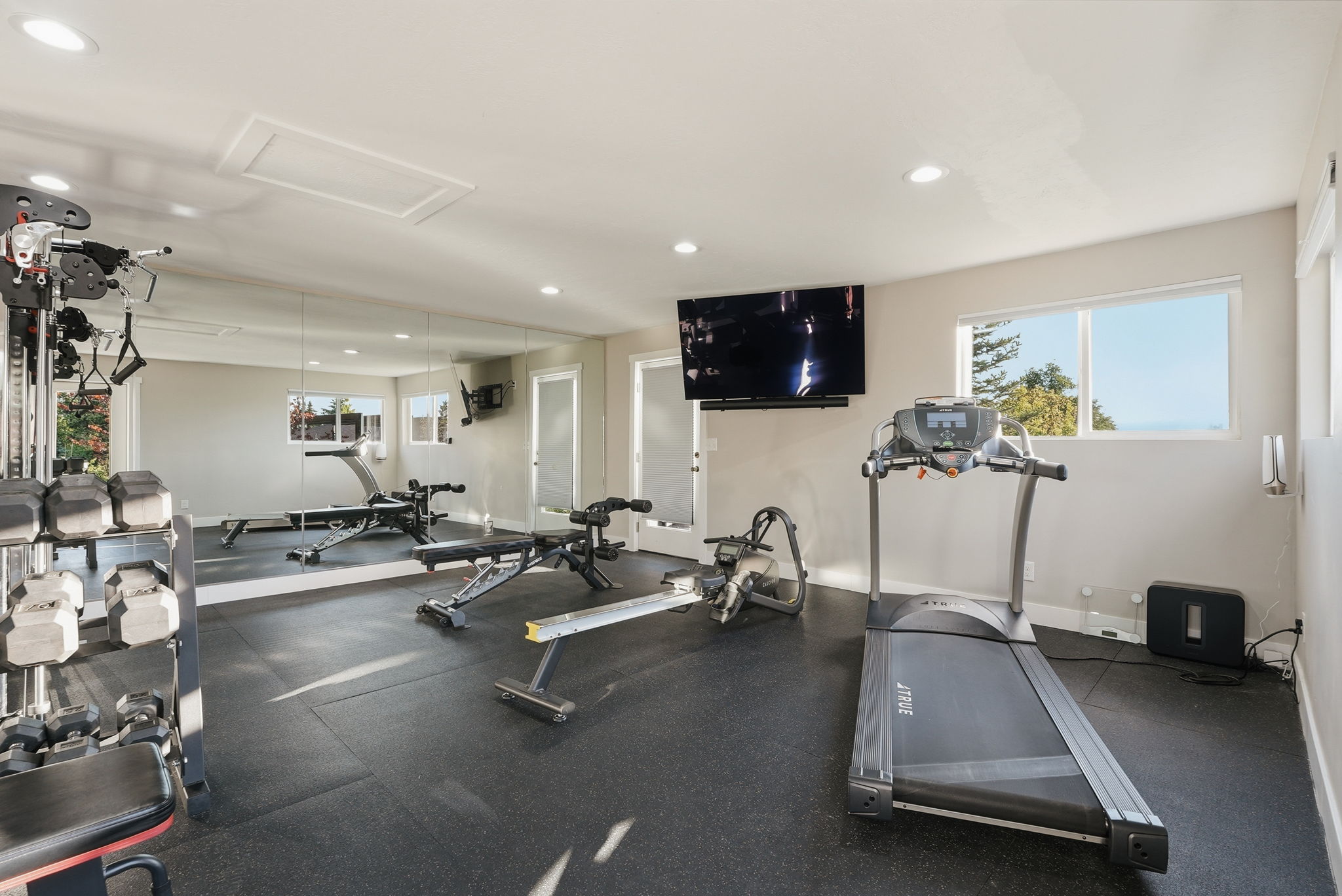 Dedicated fitness room featuring rubberized flooring, a full wall of mirrors, recessed lighting, and expansive windows