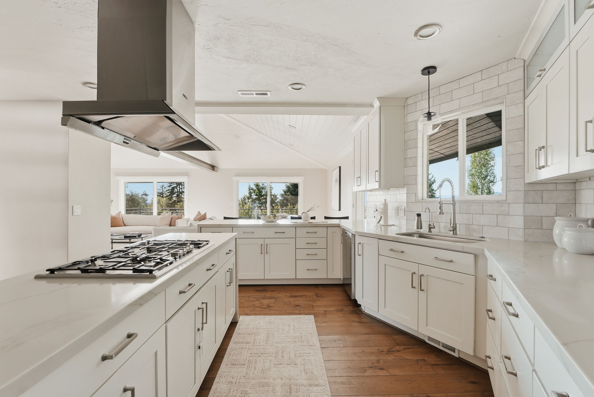 Contemporary kitchen featuring white cabinetry, light-toned countertops, a gas cooktop with a stainless steel range hood, a subway tile backsplash, and wood-finish flooring