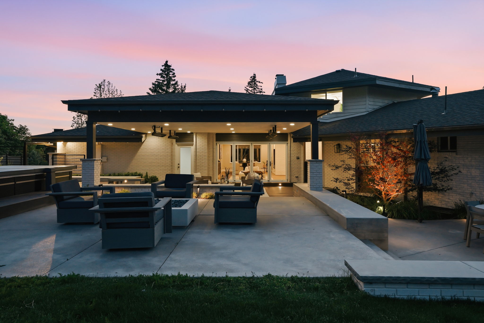 Extensive concrete patio featuring a covered outdoor living area with recessed lighting, a modern fire pit, and an elevated hot tub structure
