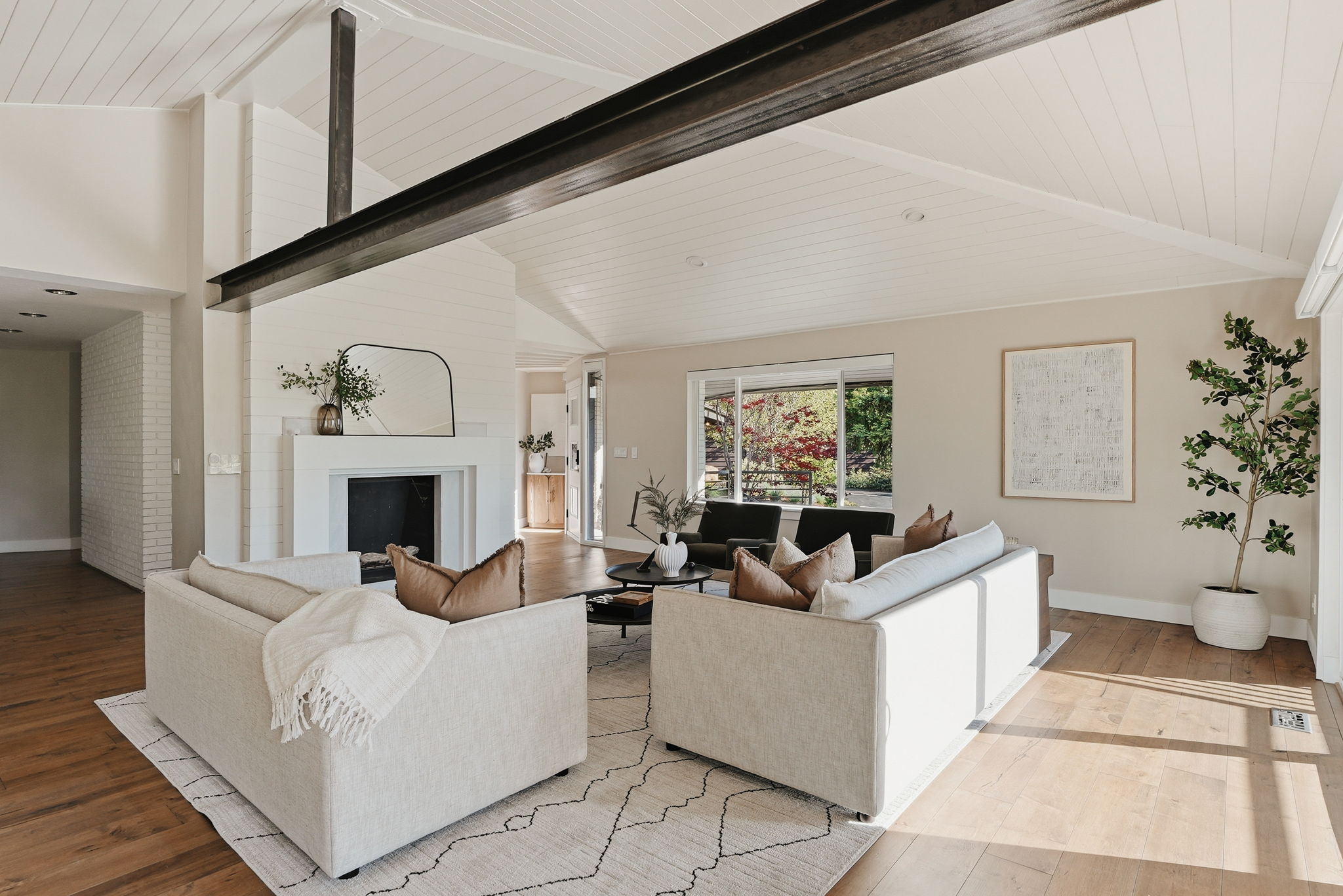 Vaulted ceilings with exposed beam, white painted brick fireplace, recessed lighting, wood-finish flooring, and expansive windows