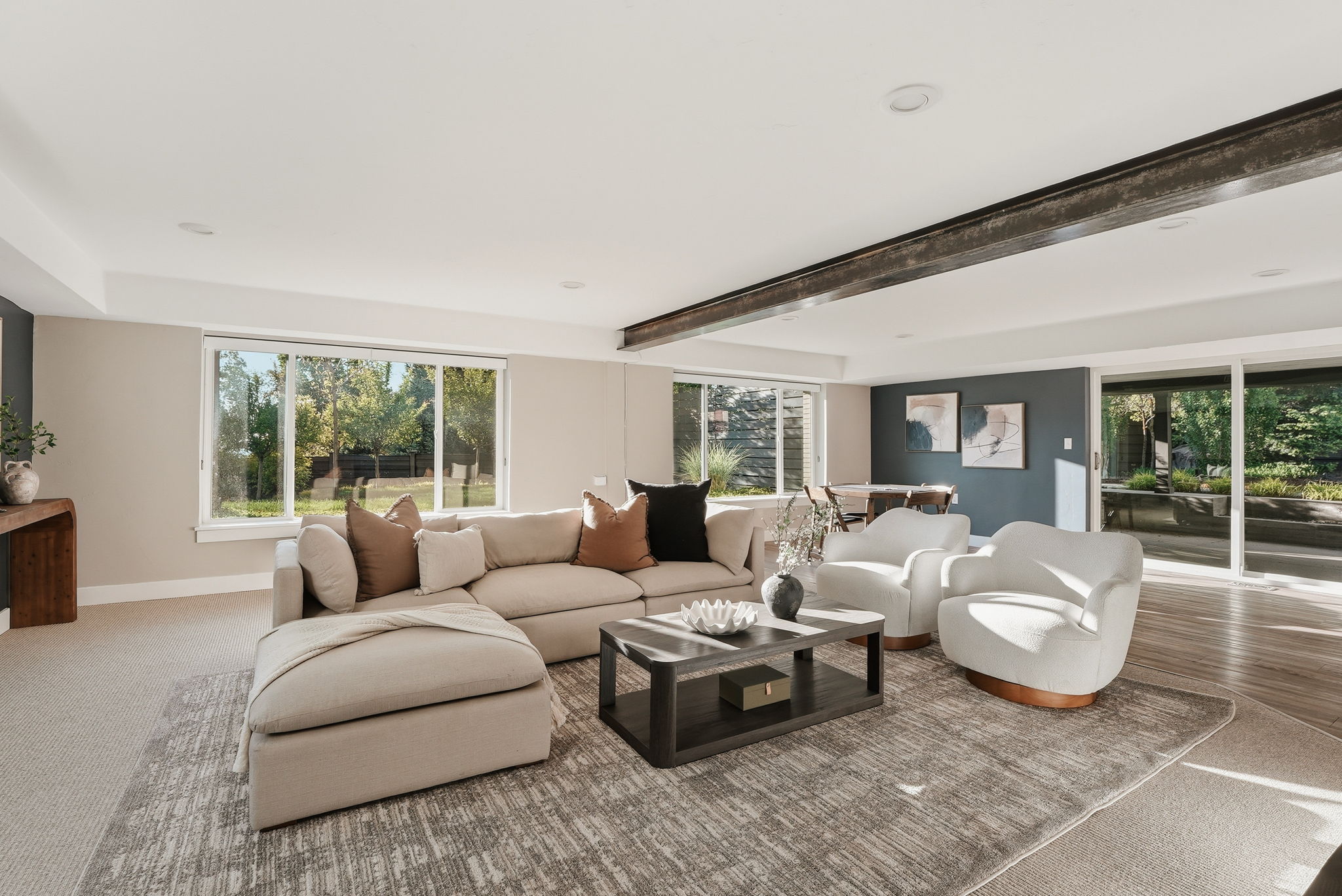 Spacious living area featuring large windows, wood-finish flooring, recessed lighting, a prominent exposed beam, and a sliding glass door