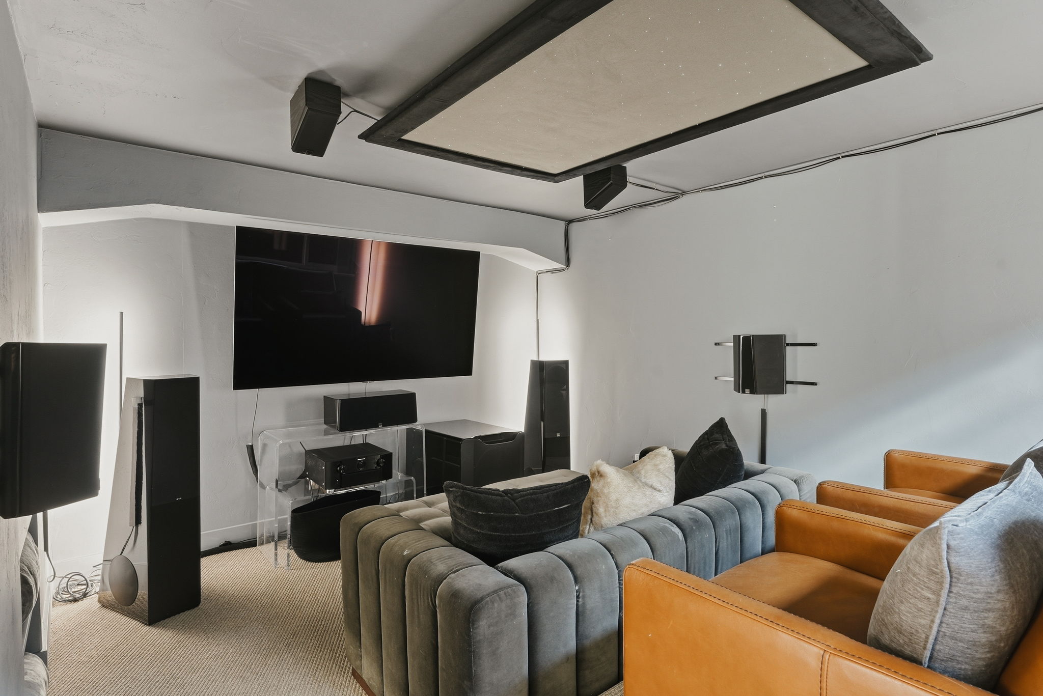 Dedicated media room featuring a large wall-mounted screen, ceiling-mounted speakers, and recessed ceiling panel