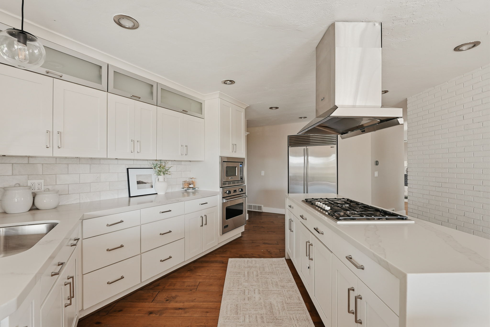 Well-appointed kitchen featuring white cabinetry, light countertops, subway tile backsplash, stainless steel appliances, and wood-finish flooring