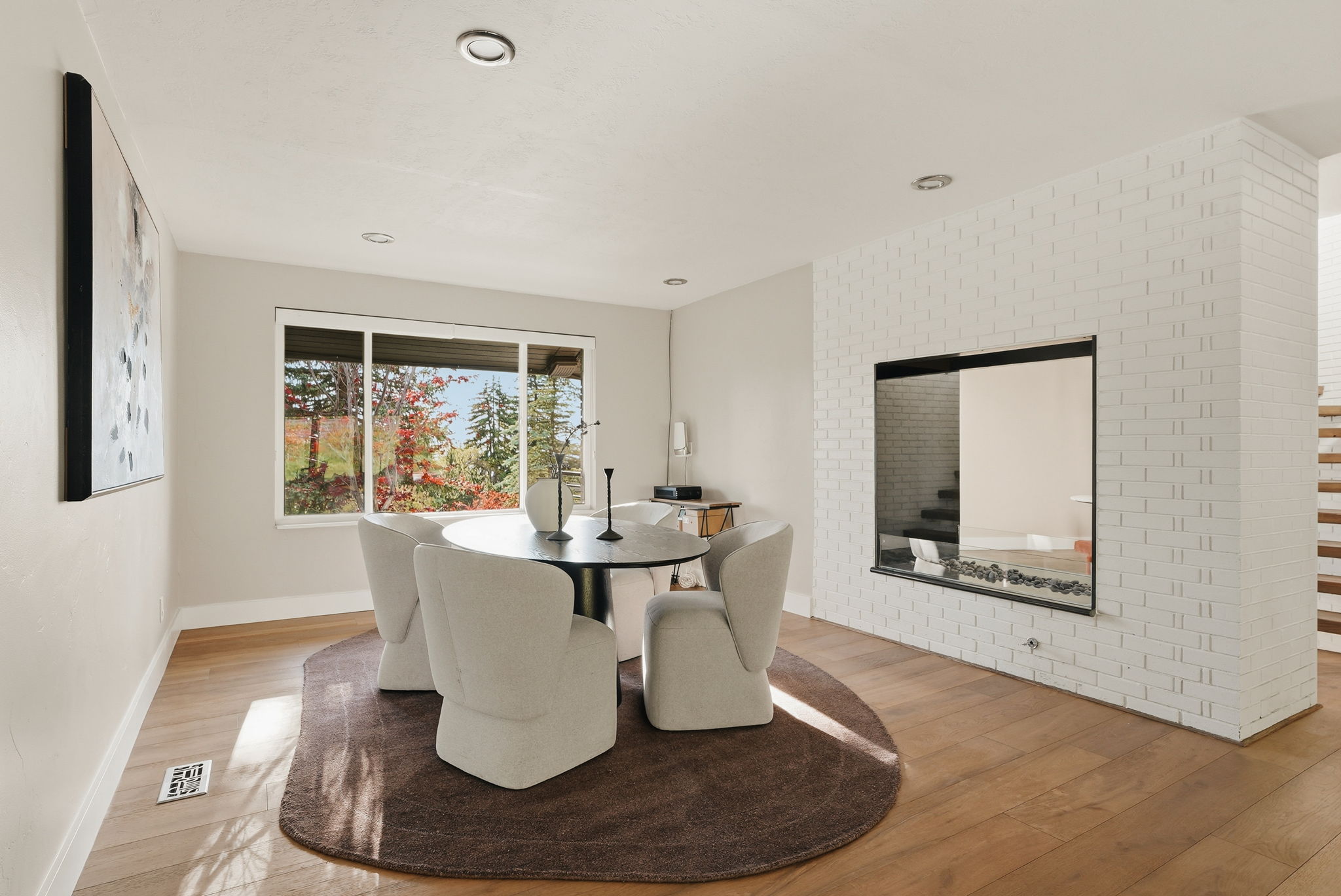 Hardwood-style flooring throughout a room featuring a modern fireplace insert with a dark frame, white brick surround, and a clear glass barrier